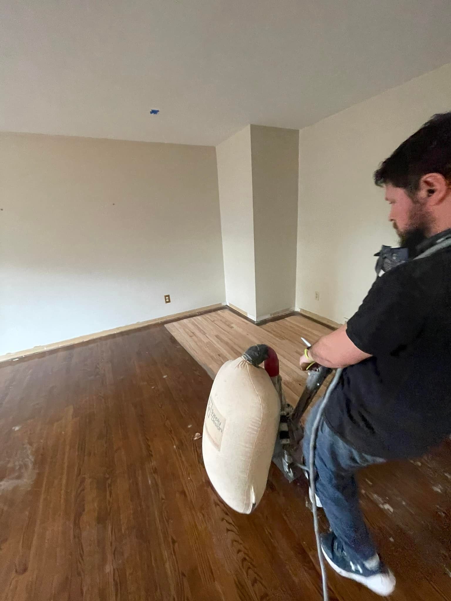 A man is sanding a wooden floor in an empty room.