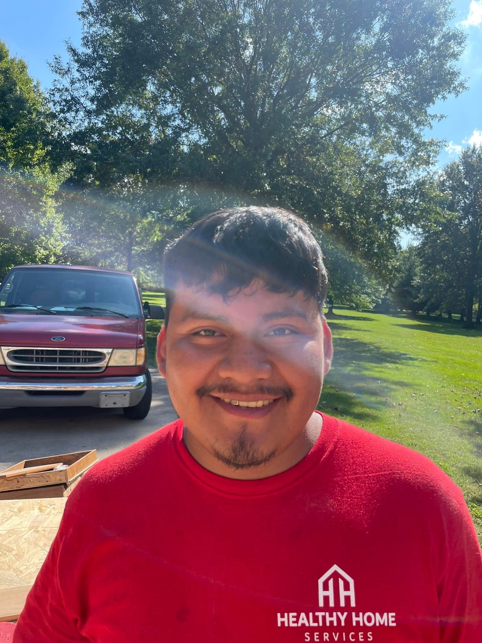 A man in a red shirt is smiling in front of a red van.