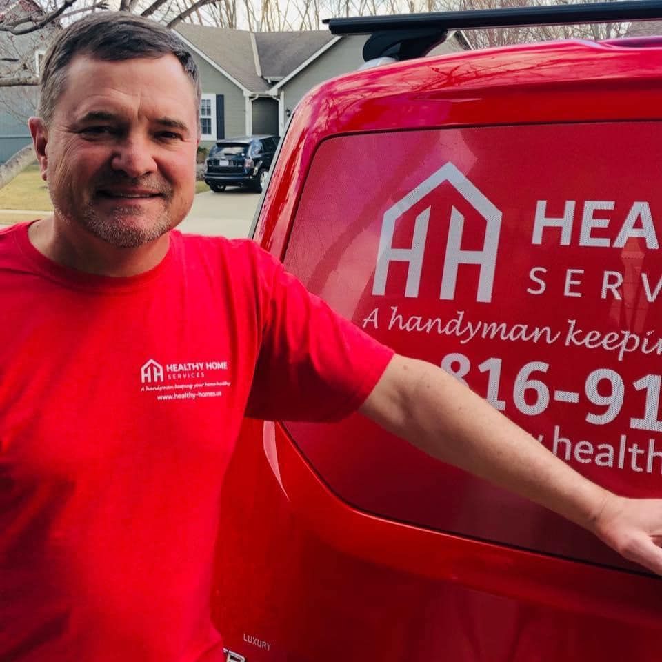 A man in a red shirt is standing in front of a red van that says hear serve