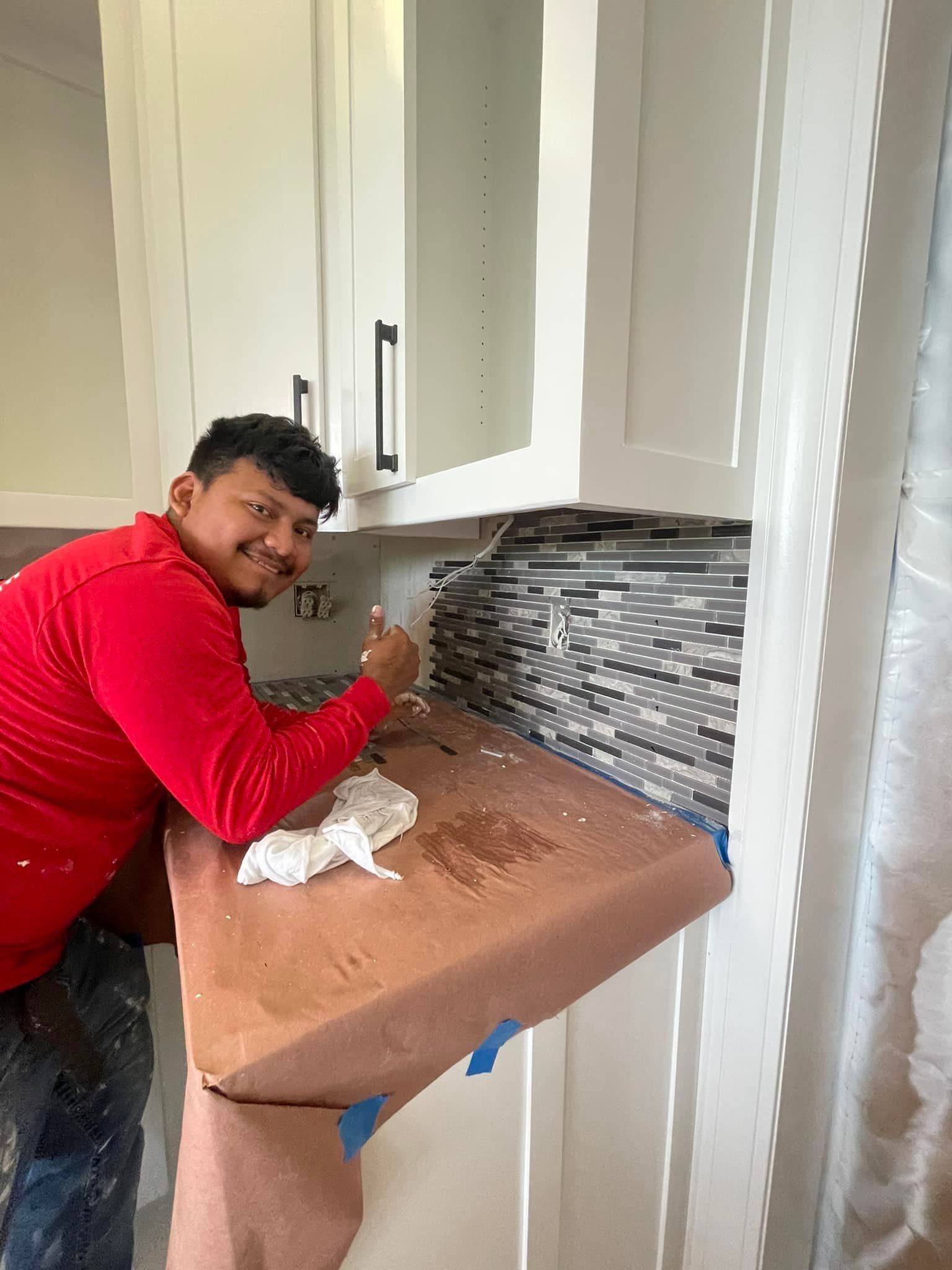 A man in a red shirt is sitting at a counter in a kitchen.