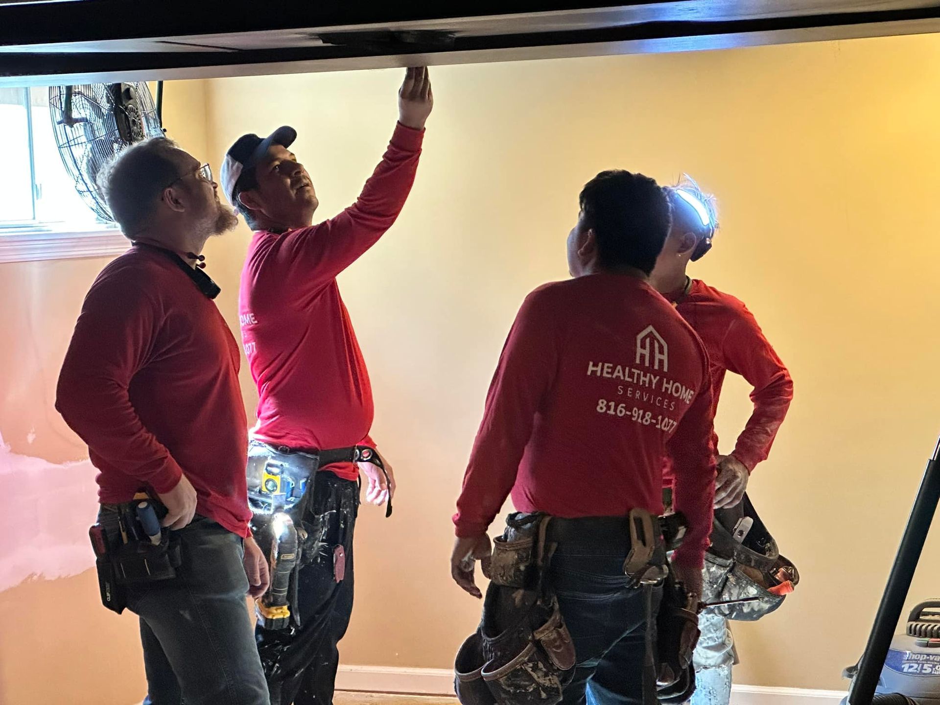 A group of men in red shirts are working on a ceiling.
