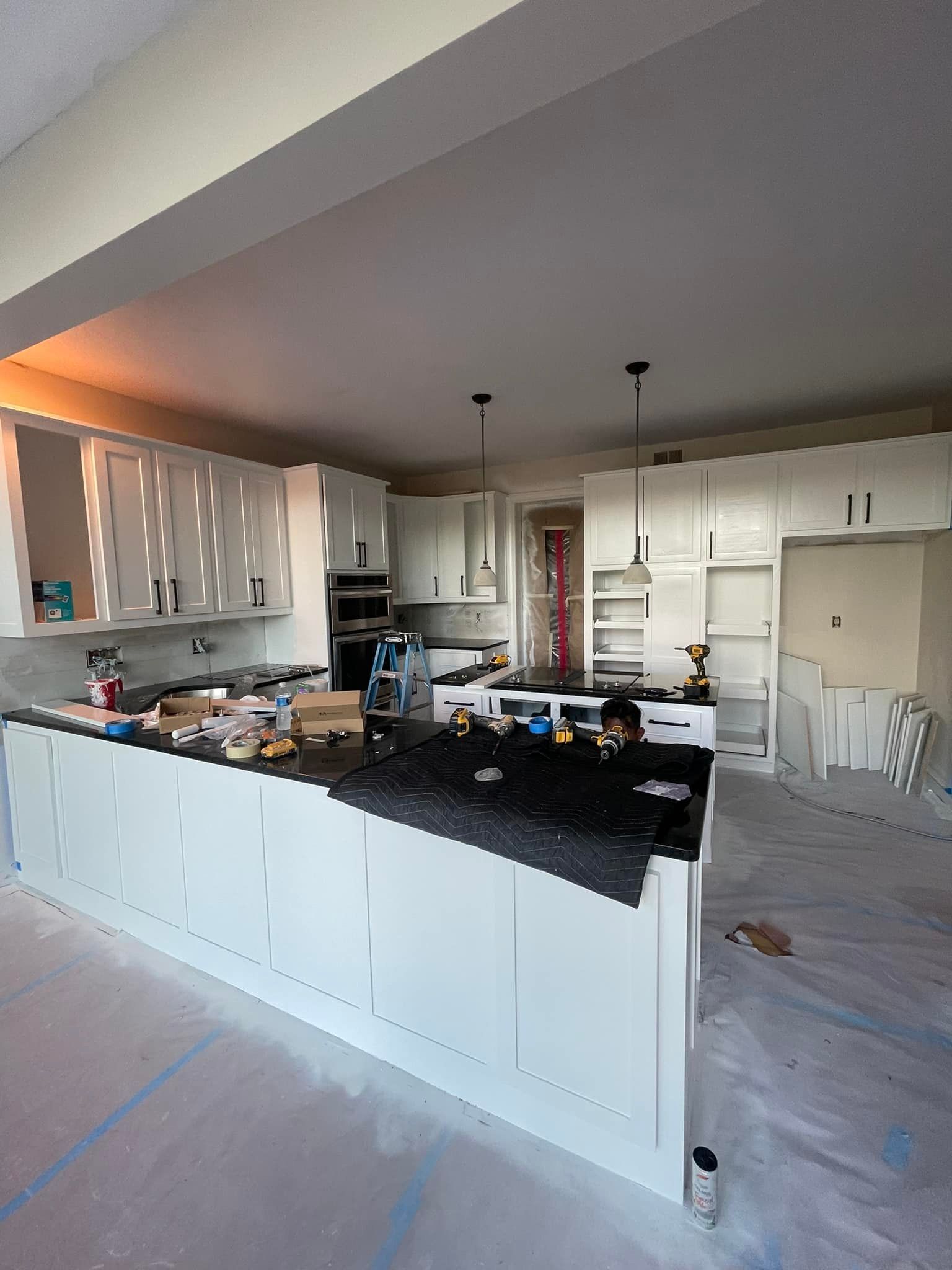 A kitchen under construction with white cabinets and a black counter top.