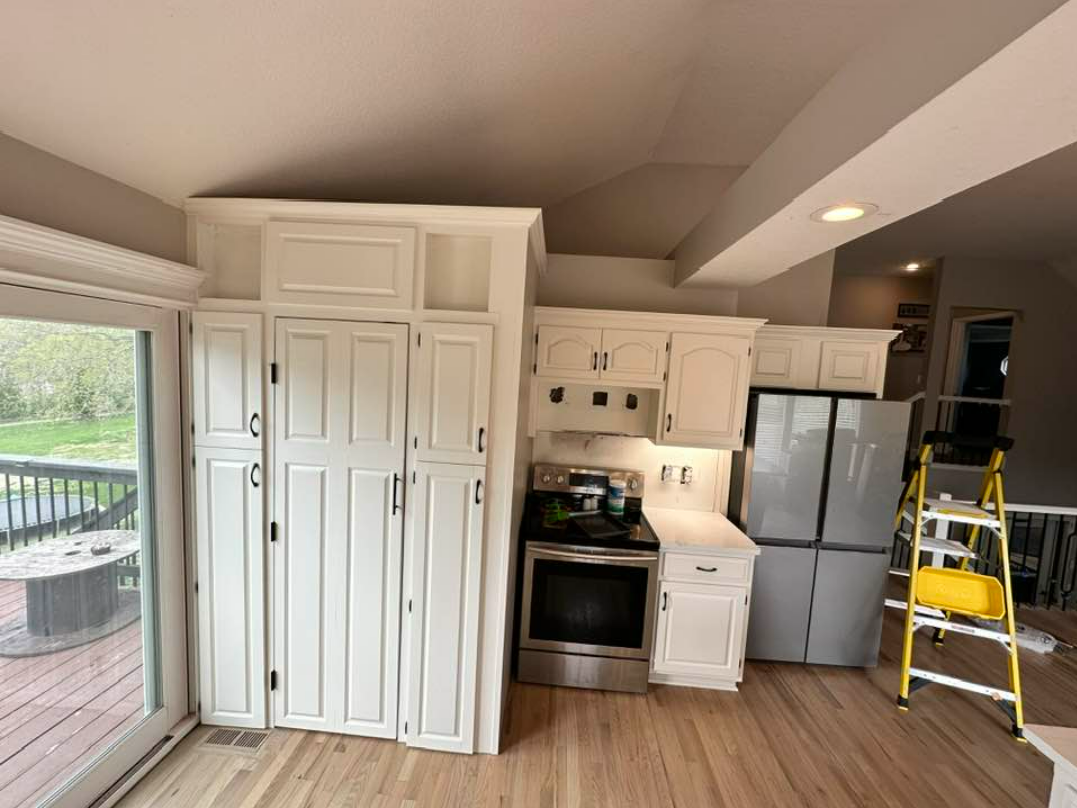 A kitchen with white cabinets , stainless steel appliances , a refrigerator and a ladder.