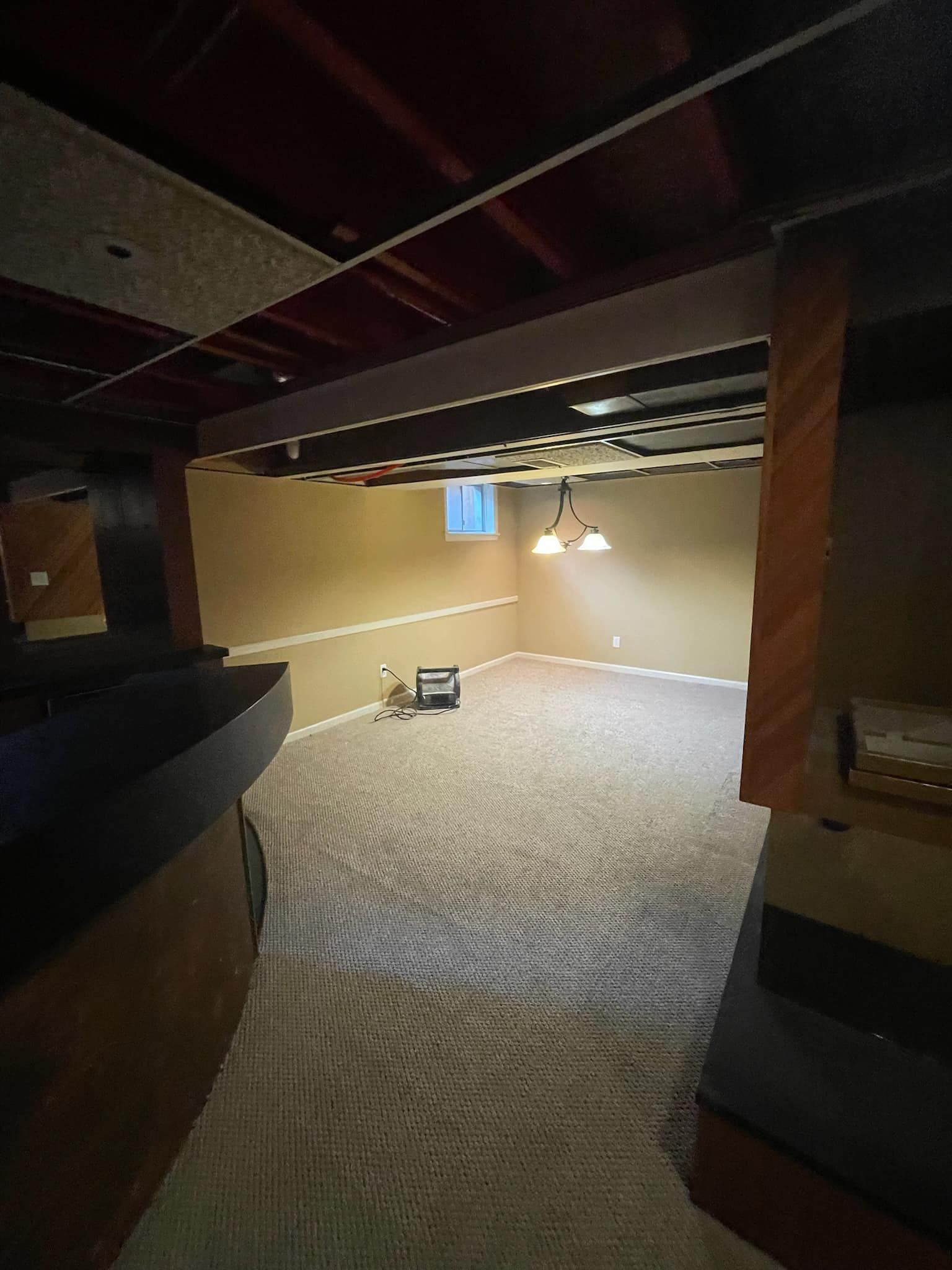 An empty basement with a carpeted floor and a bar.