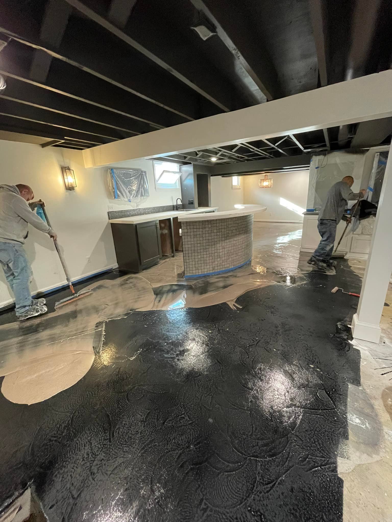 Two men are painting a black floor in a basement.