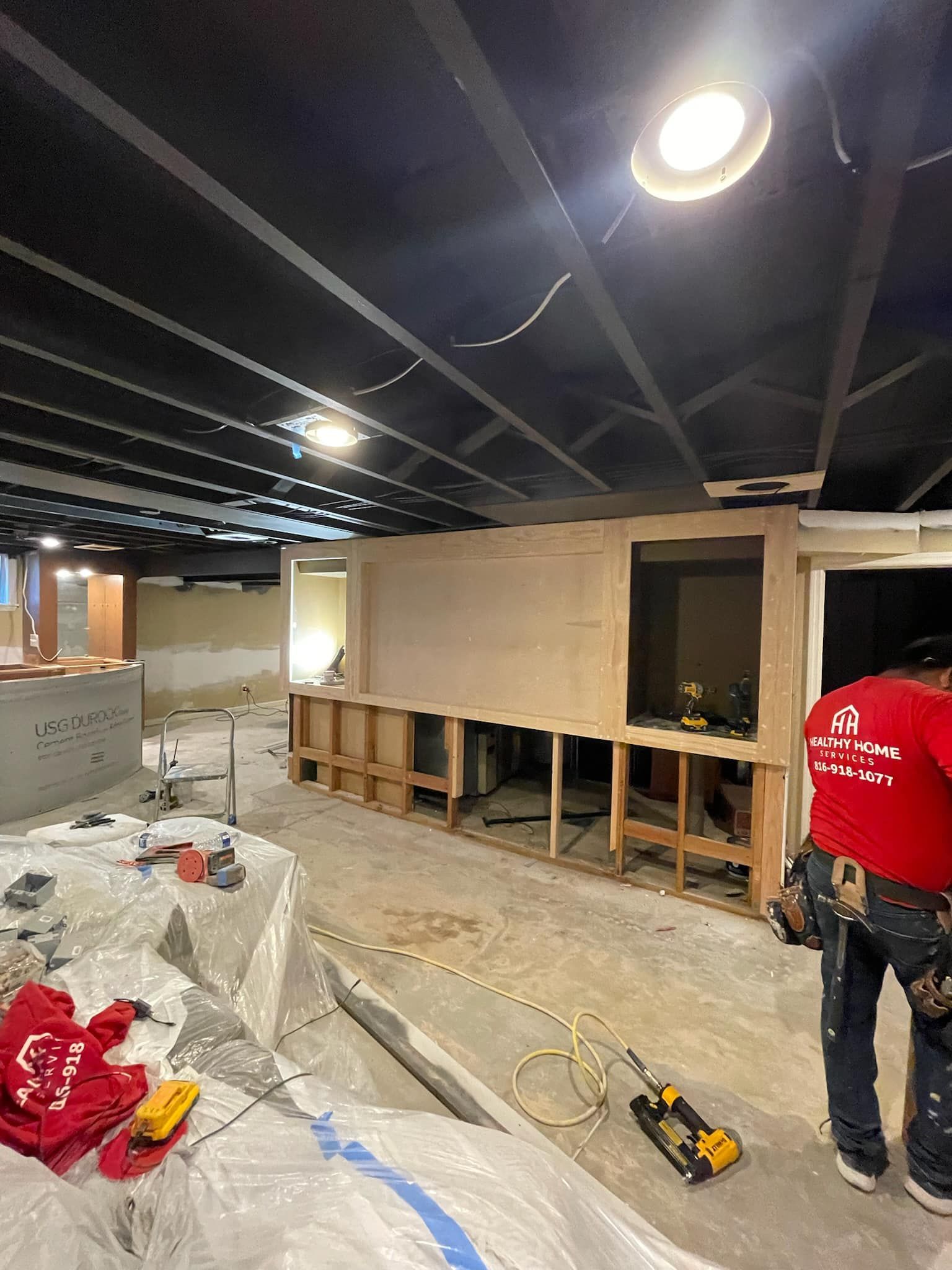 A man in a red shirt is standing in a room under construction.