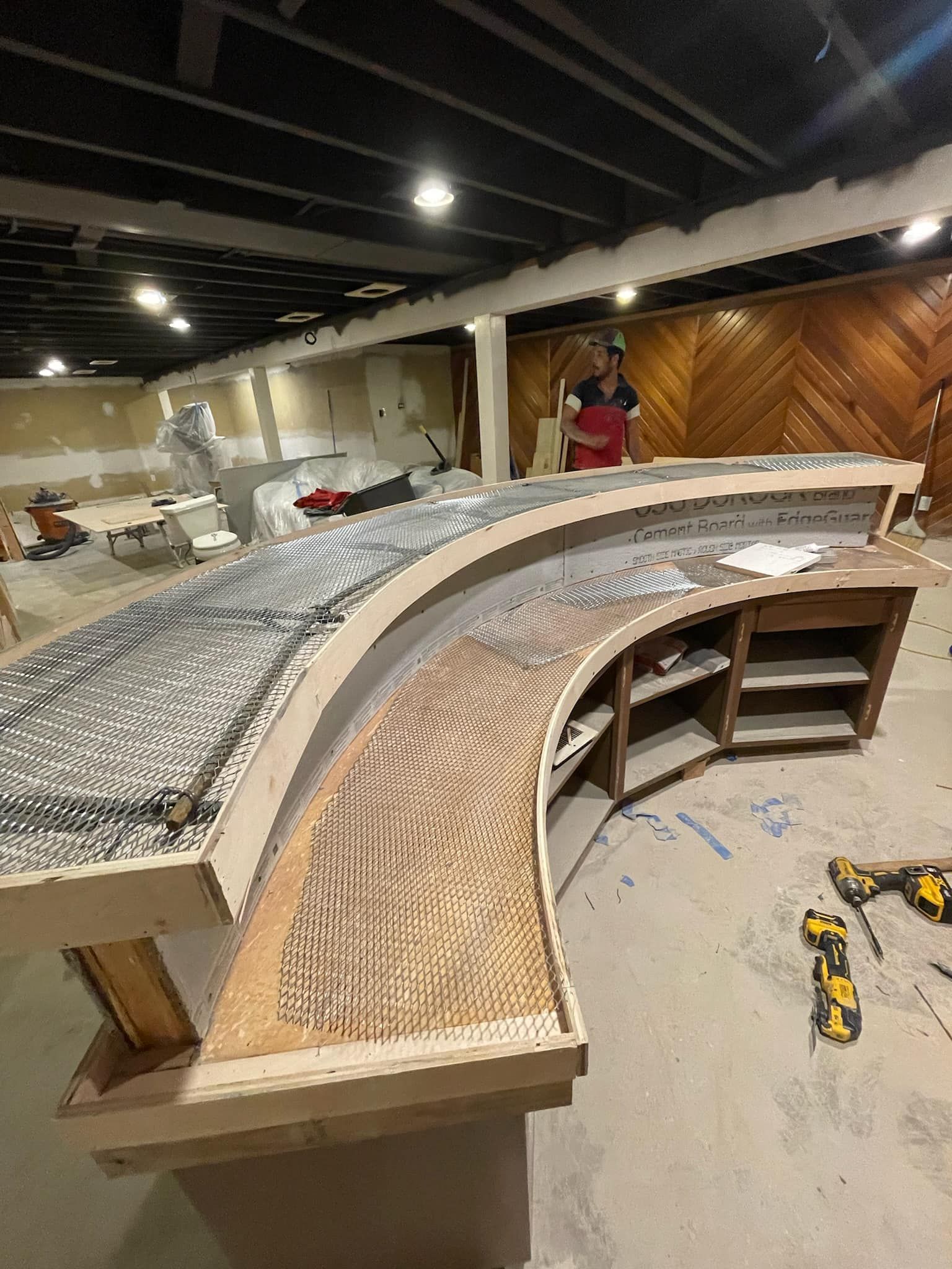 A man is standing next to a curved wooden table in a room.