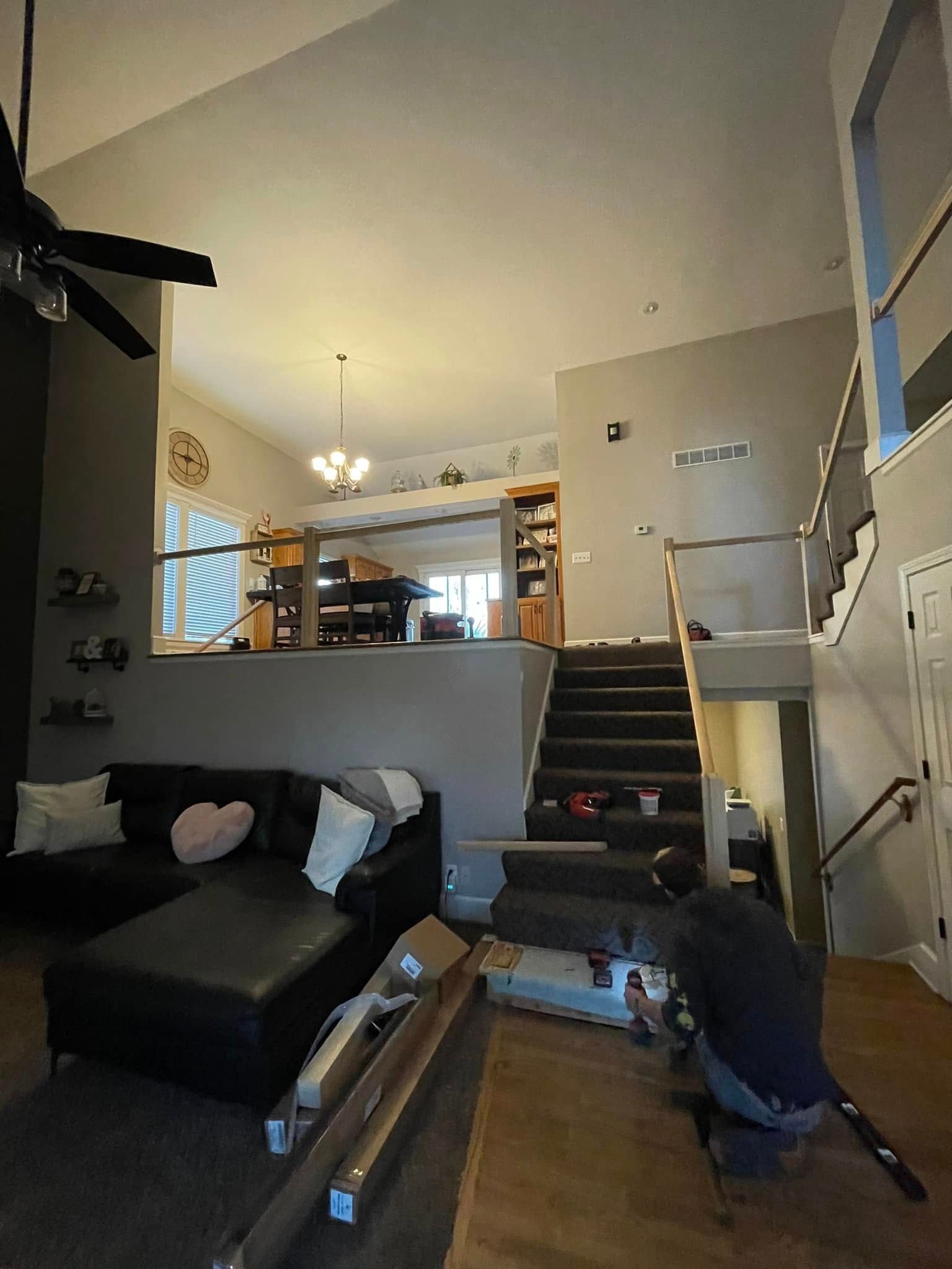 A man is kneeling in a living room next to a couch and stairs.