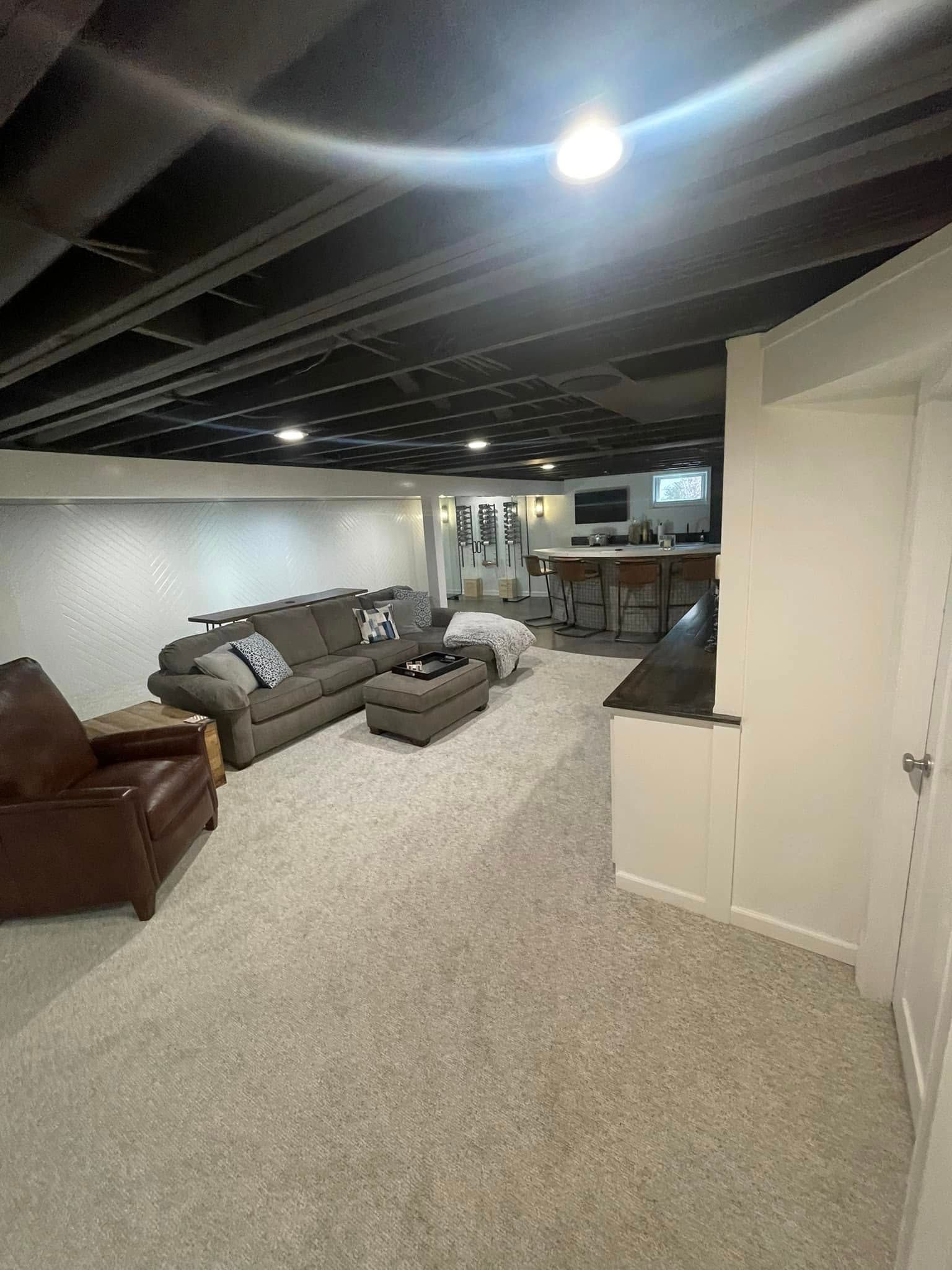 A living room in a basement with a couch , chair and ottoman.