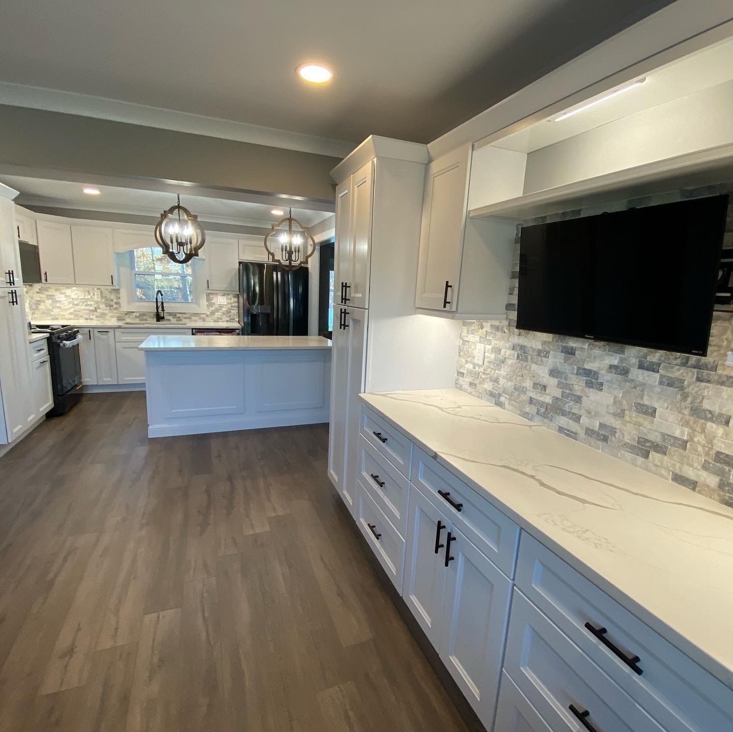 A kitchen with white cabinets and a flat screen tv
