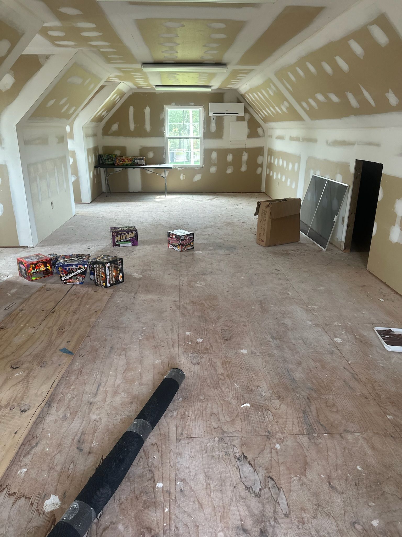 Attic room under construction with exposed floorboards, drywall, and a window.