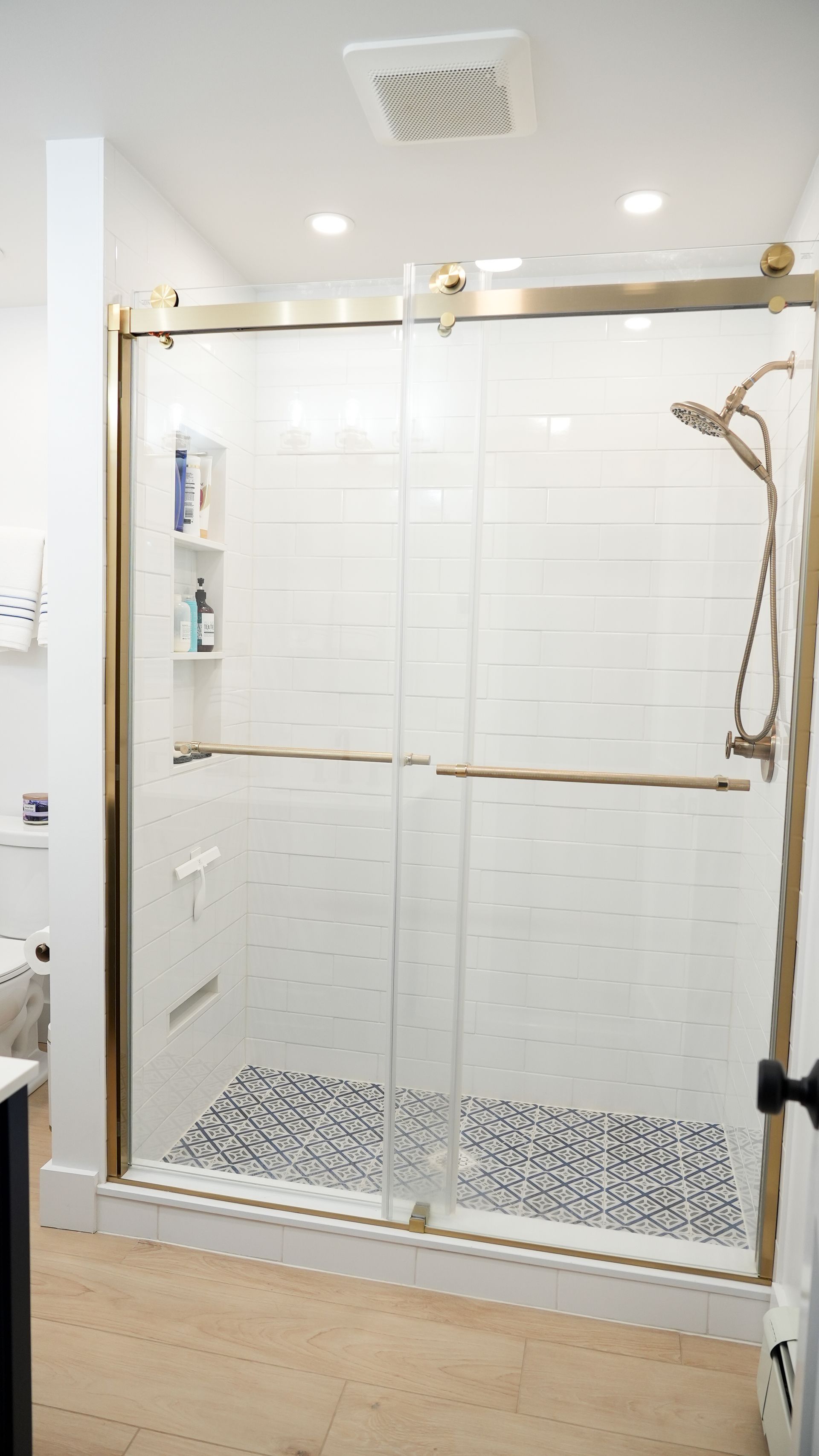 Modern shower with gold trim, white subway tile, and pebble tile floor.