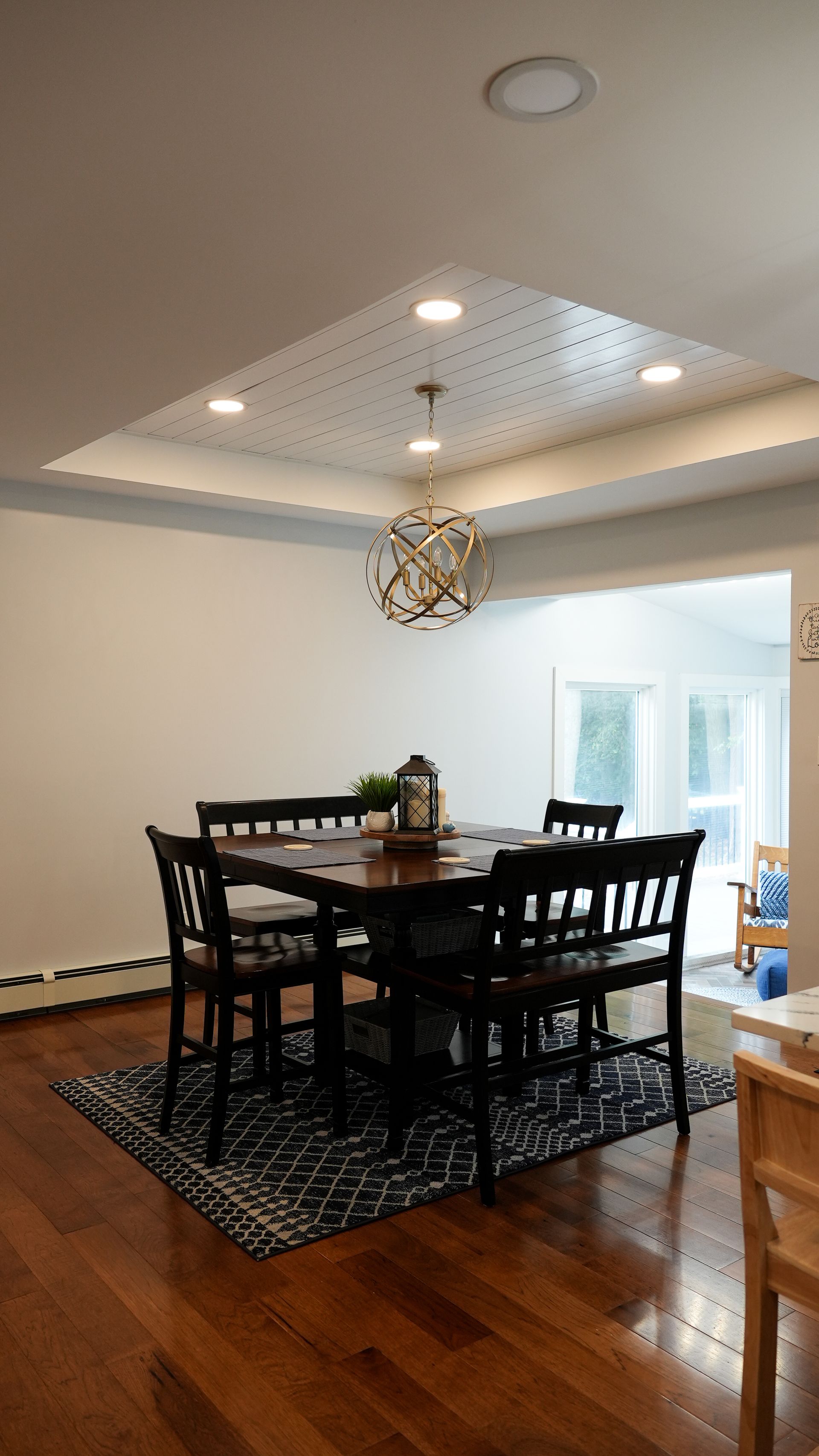 Dining room with a dark wooden table, black chairs, and a patterned rug under a textured ceiling.
