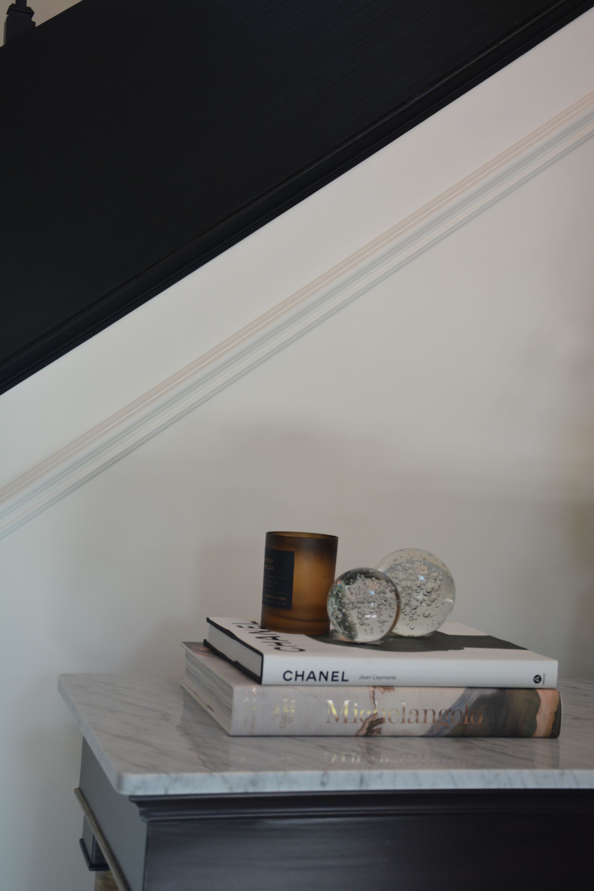 Marble-topped table with books, candle, and decorative spheres, set against a black and white staircase.