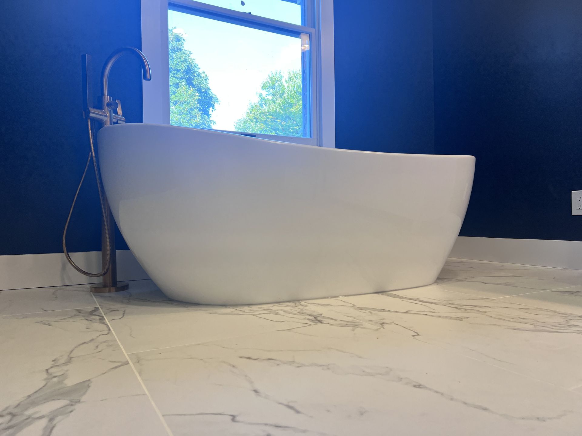 A white bathtub is sitting on a tiled floor in a bathroom next to a window.