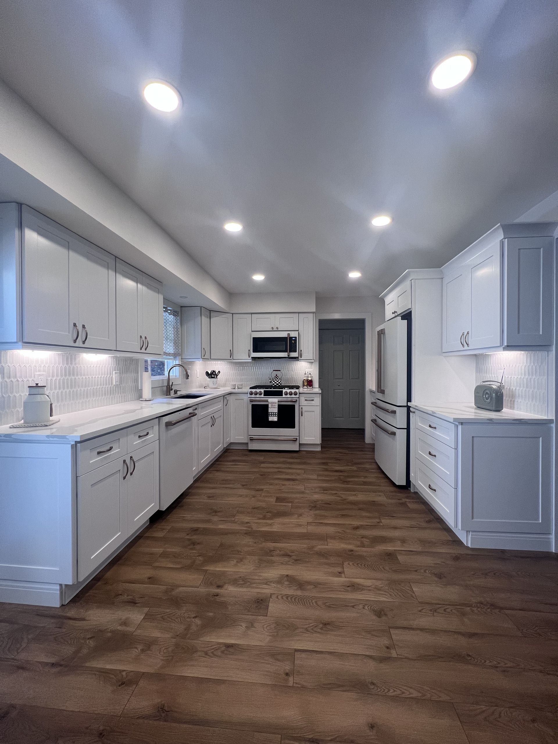 A kitchen with white cabinets and wooden floors.