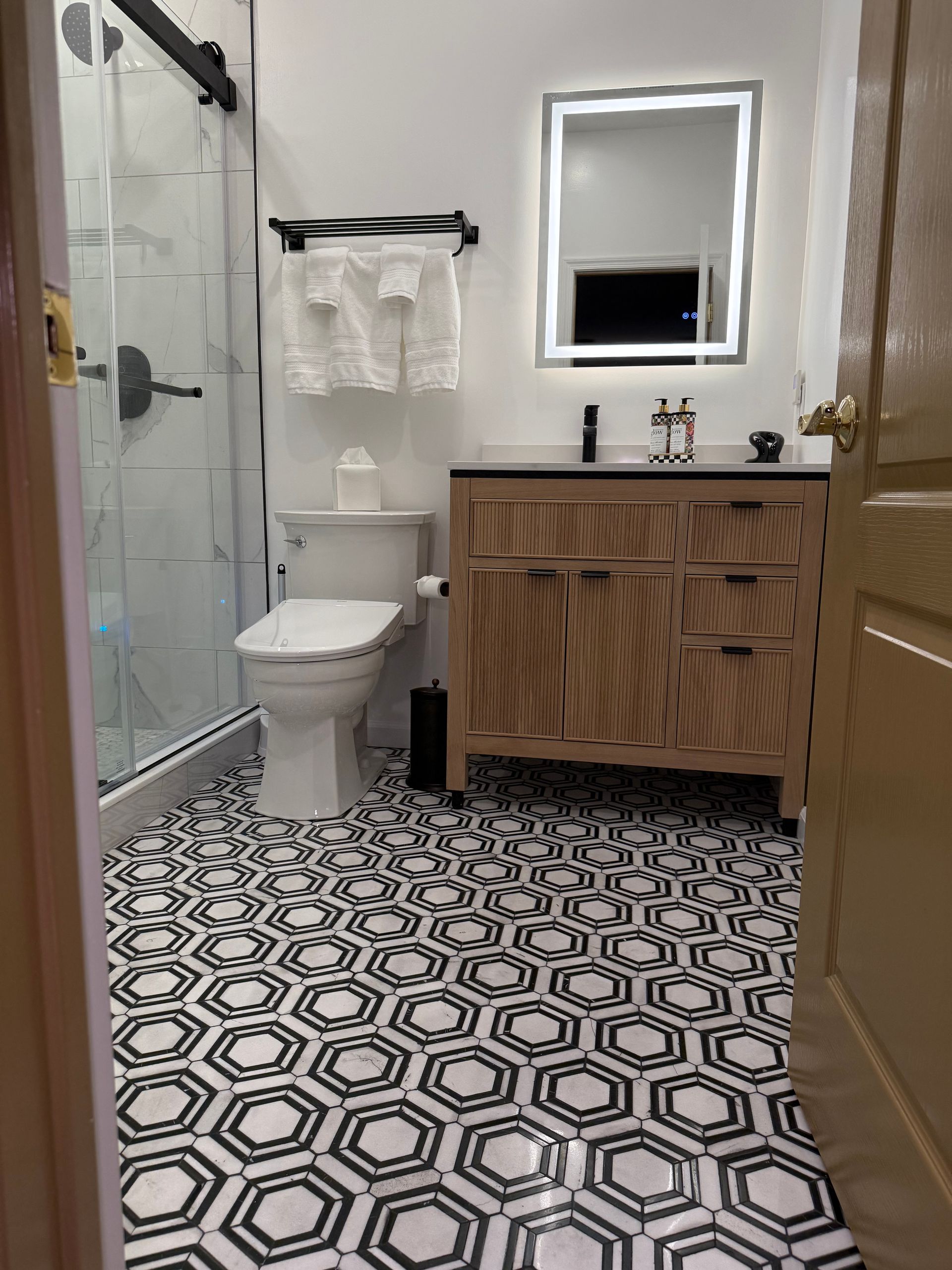 Bathroom with black and white hexagonal floor tiles, shower, vanity, and toilet.
