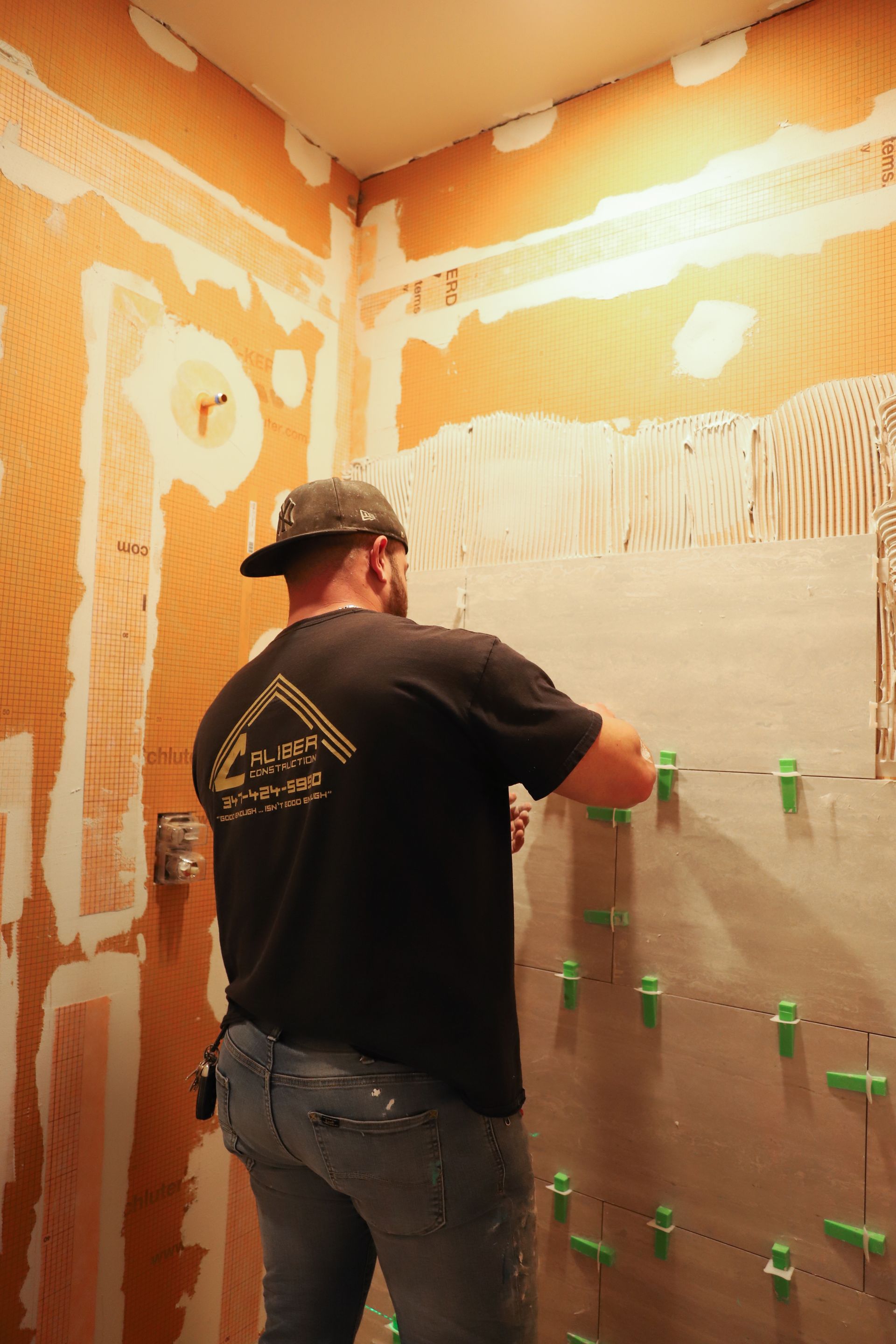A man is laying tiles on a wall in a bathroom.
