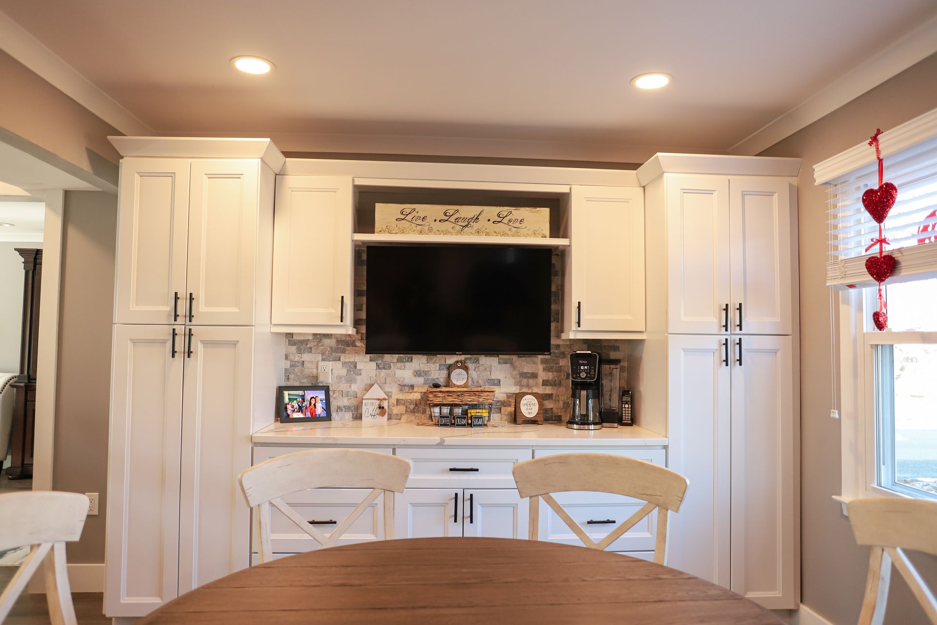 A kitchen with white cabinets and a flat screen tv on the wall.