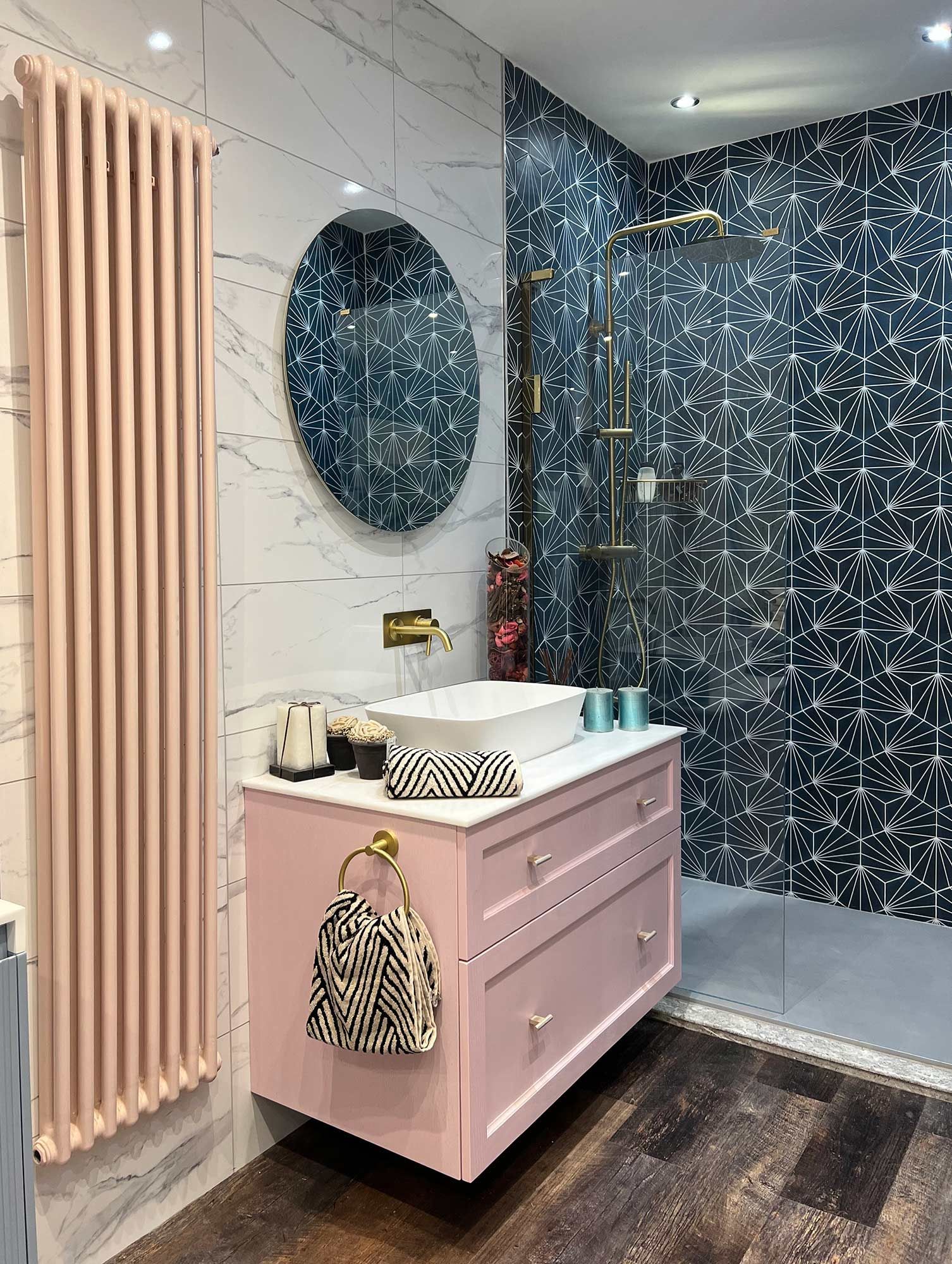 A bathroom with a pink vanity and a round mirror