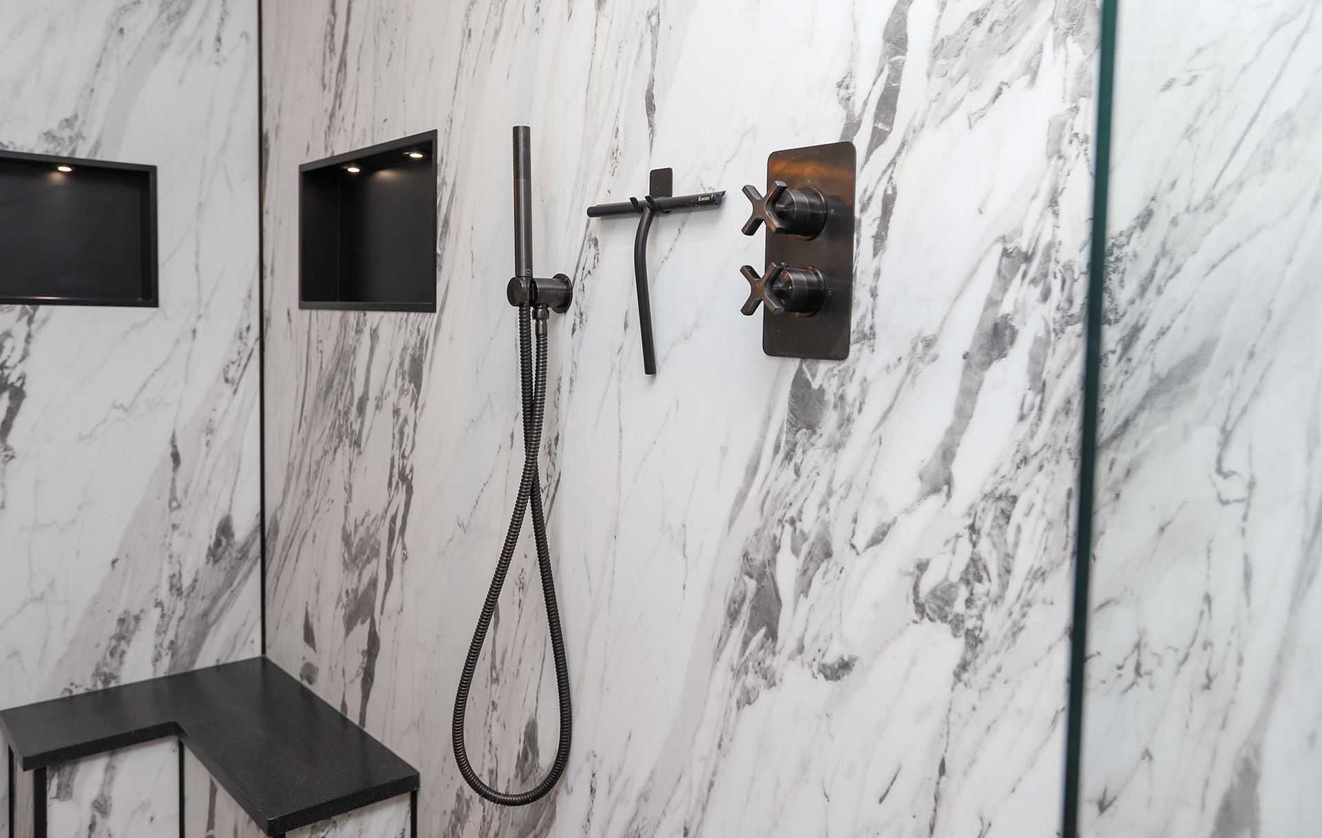 A shower with a black shower head and a cross on the wall.