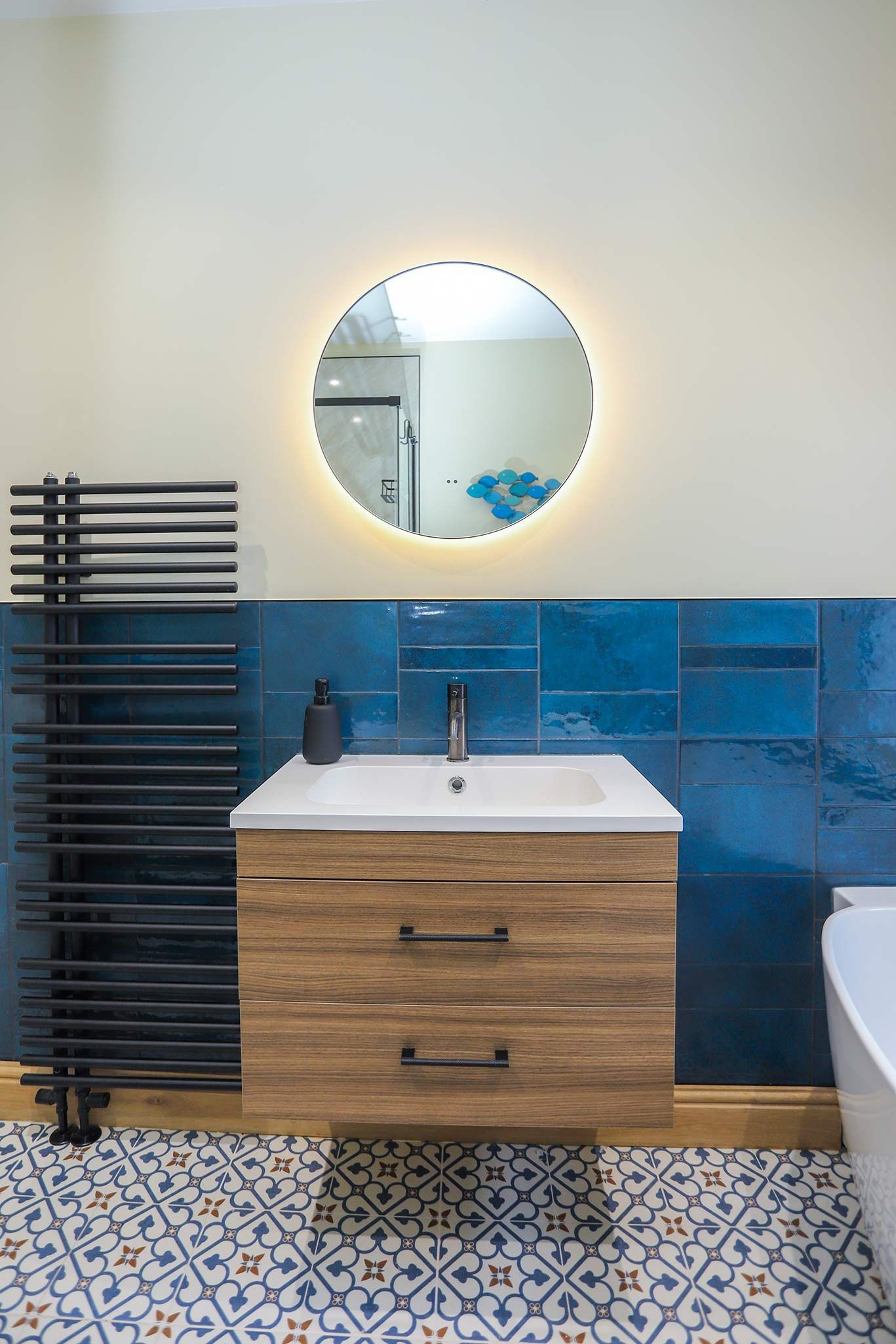 A bathroom with blue tiles and a round mirror