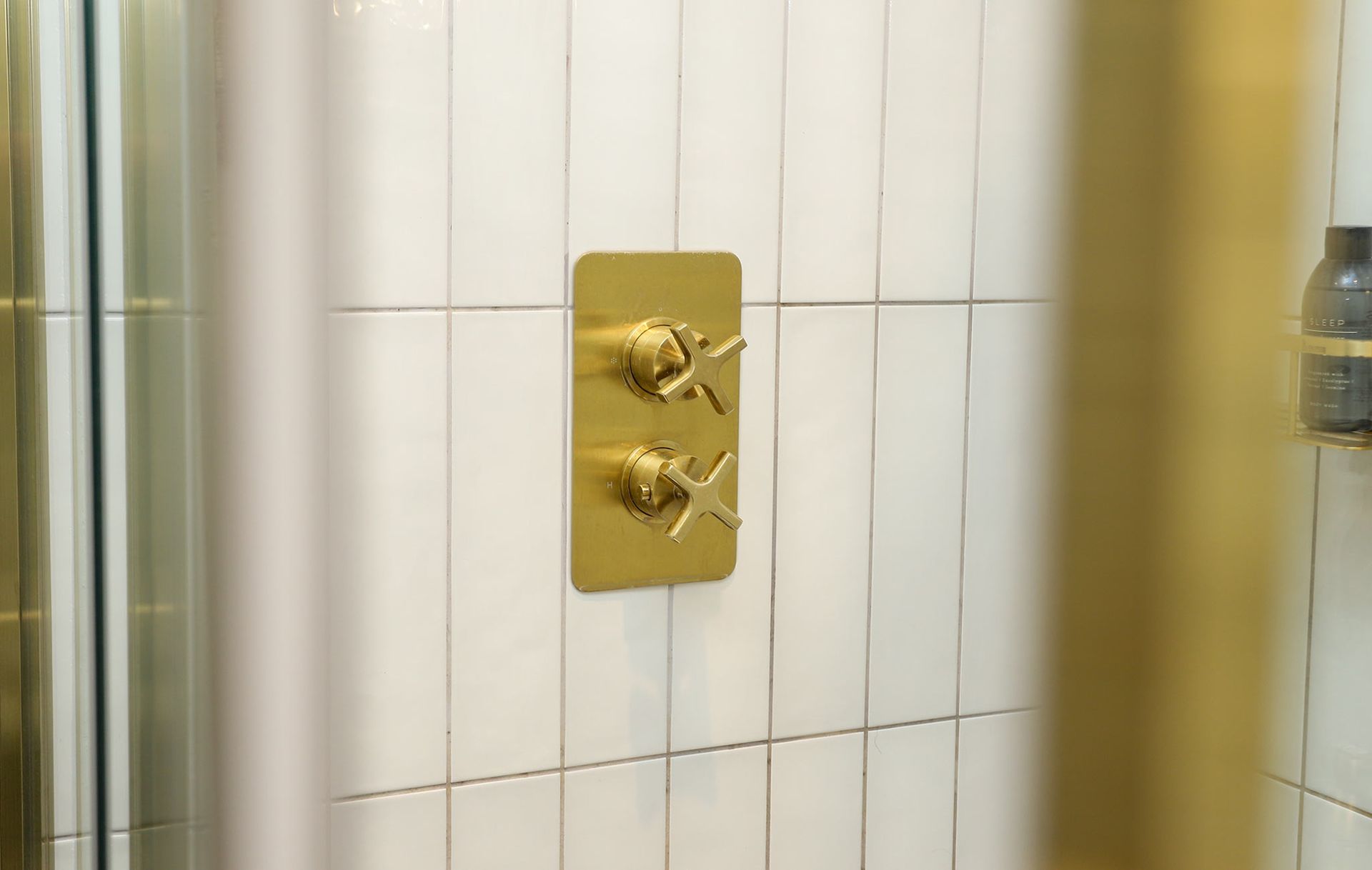 A bathroom with white tiles and a gold shower head