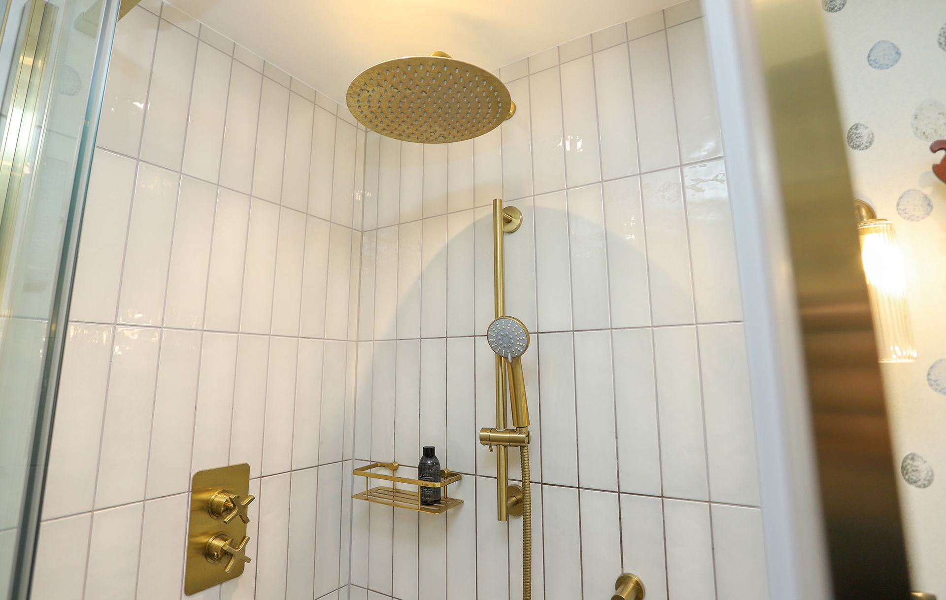 A bathroom with white tiles and a gold shower head