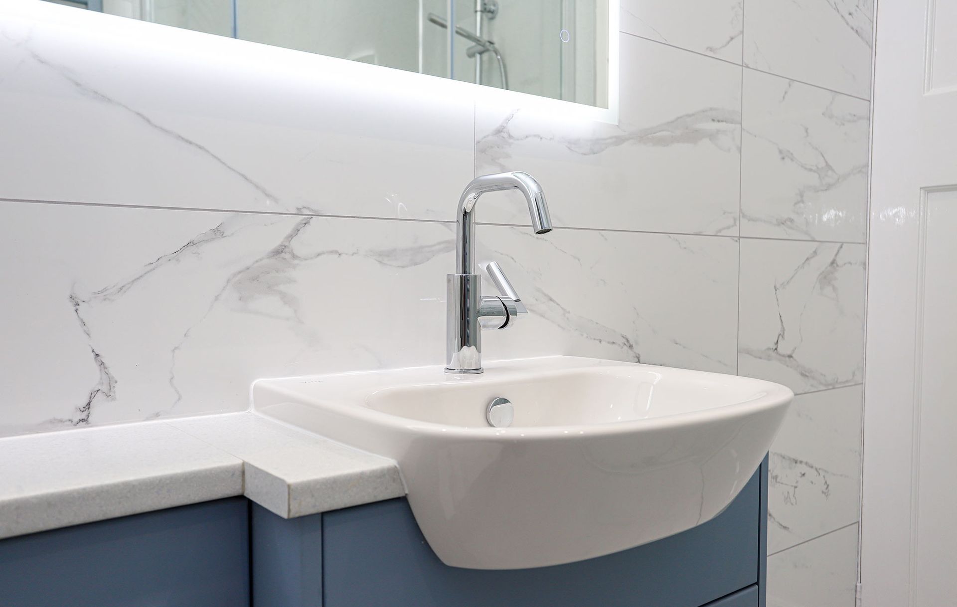 A bathroom with a sink , mirror and marble wall.