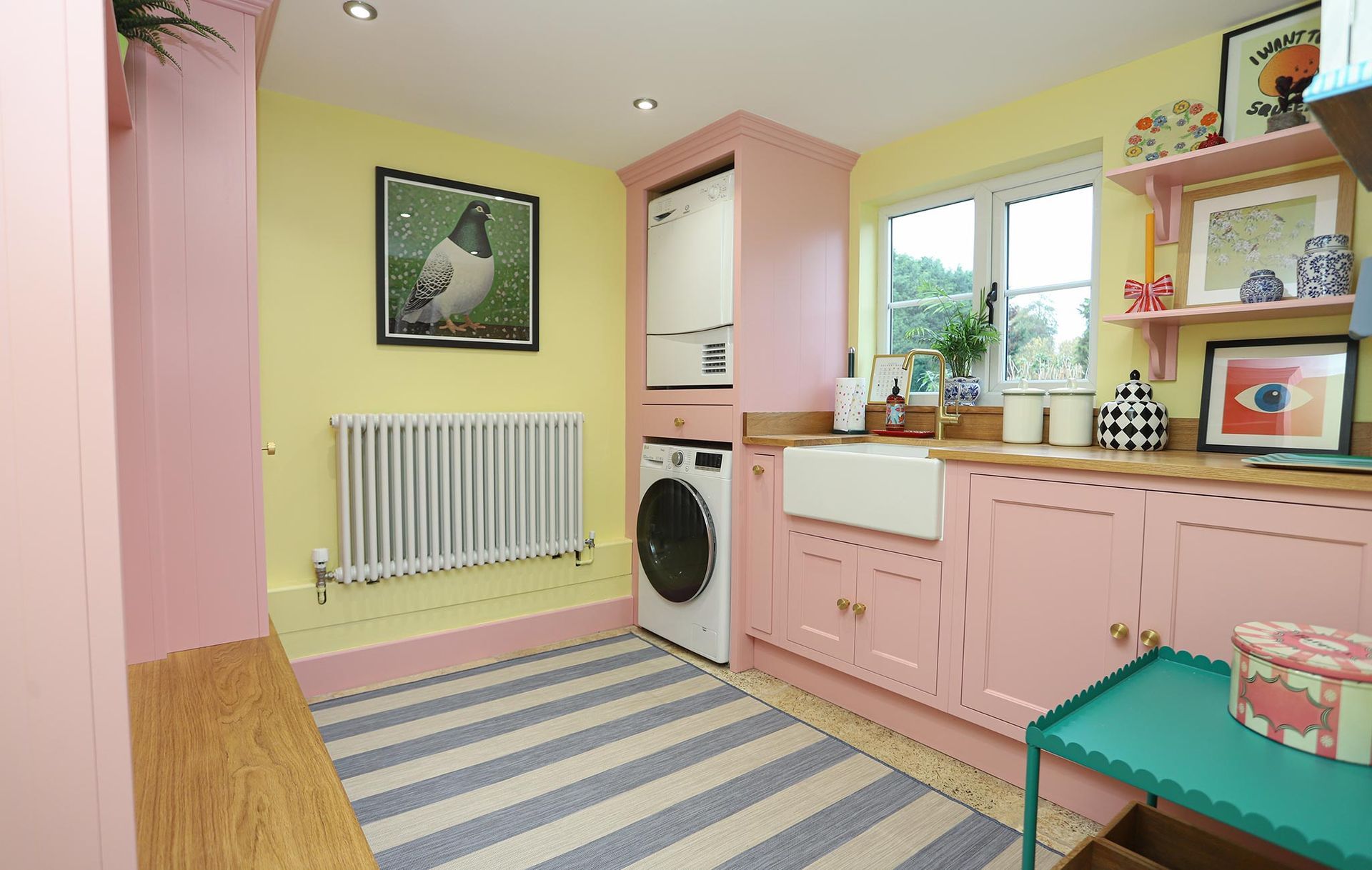 A laundry room with pink cabinets and a striped rug