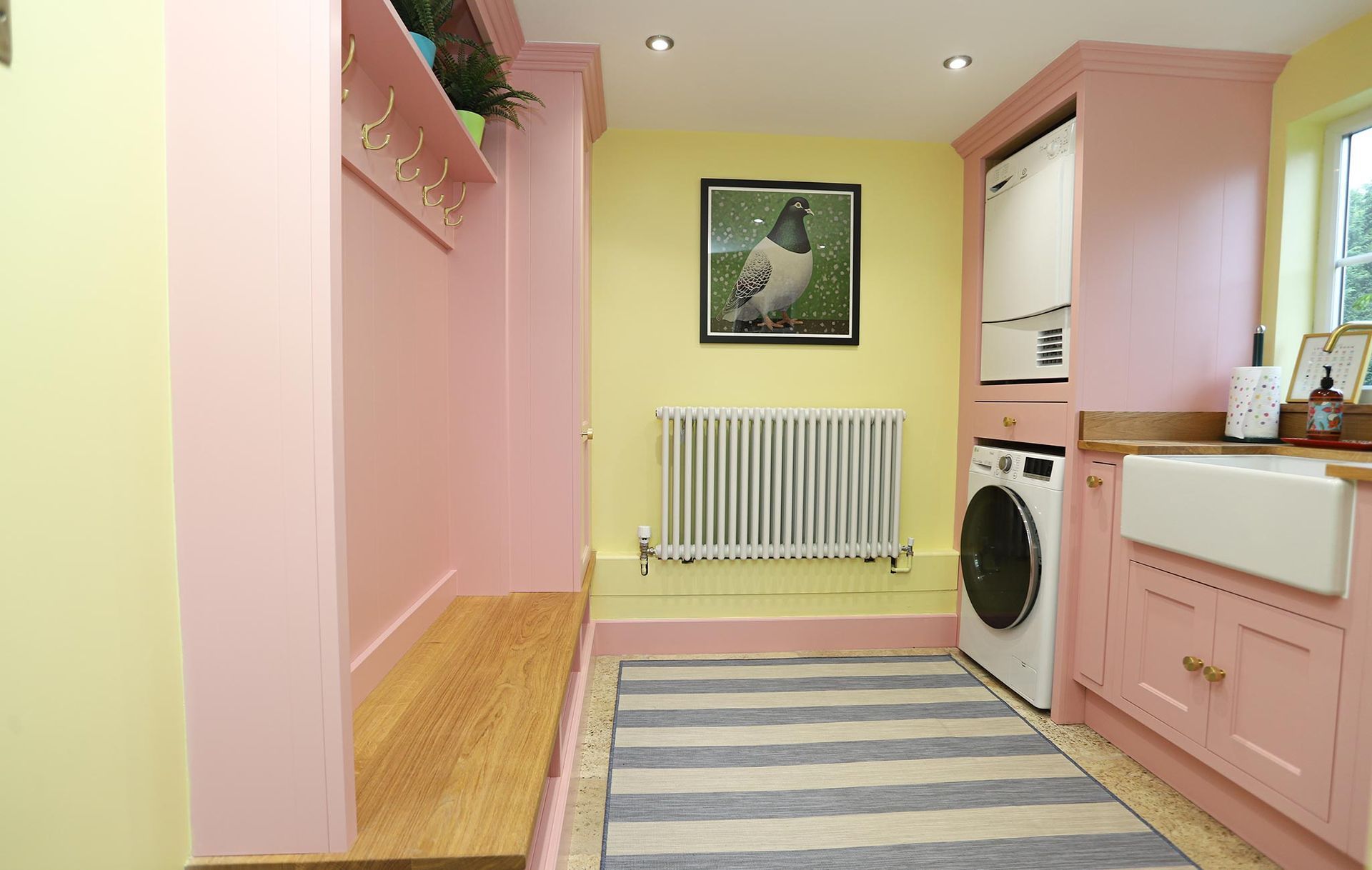 A laundry room with pink cabinets and a striped rug