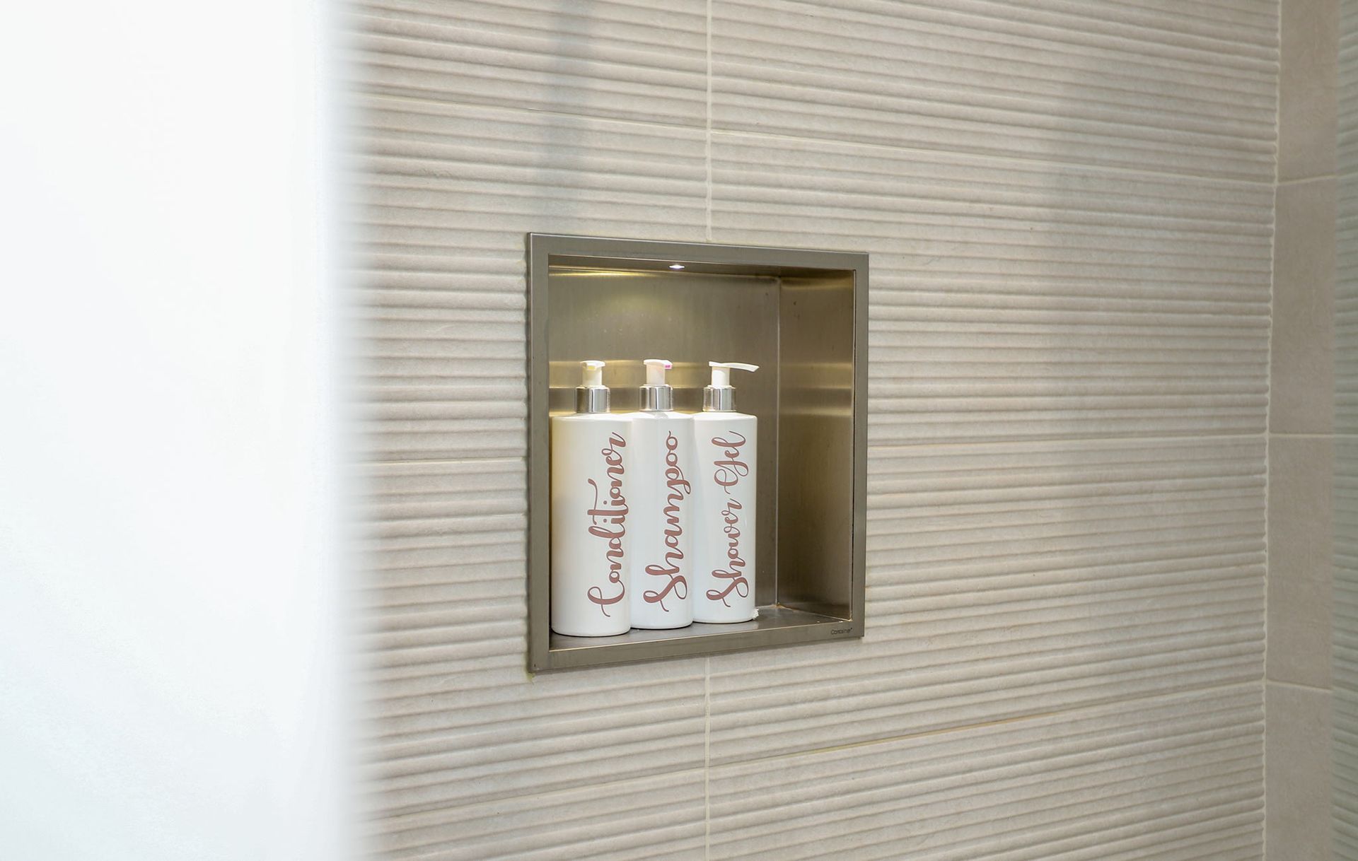Three bottles of conditioner and shampoo are in a shower niche