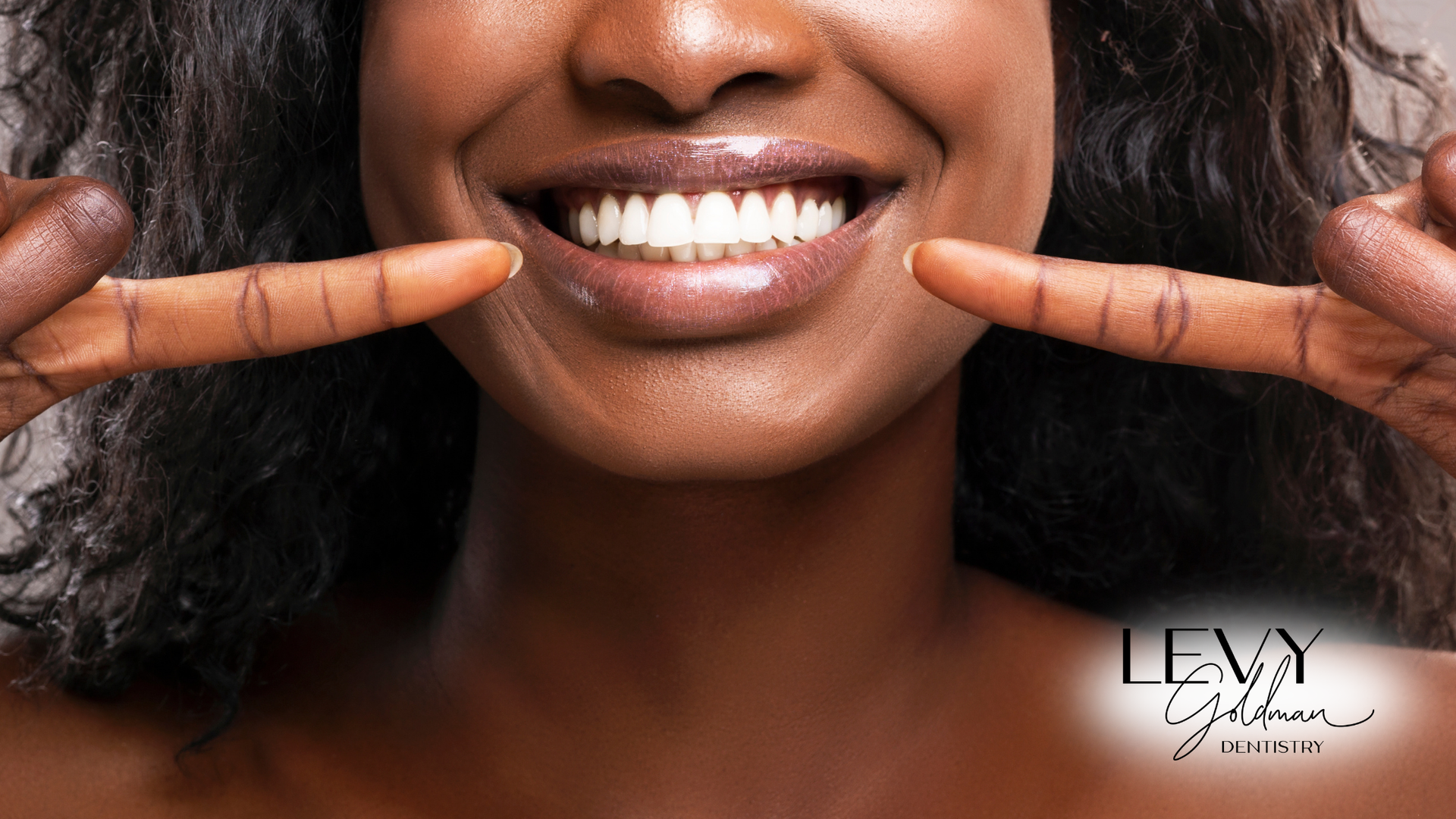 A woman is smiling and pointing at her teeth with her fingers.