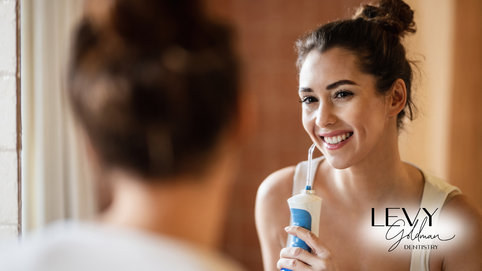 A woman is smiling while using an electric toothbrush in front of a mirror.