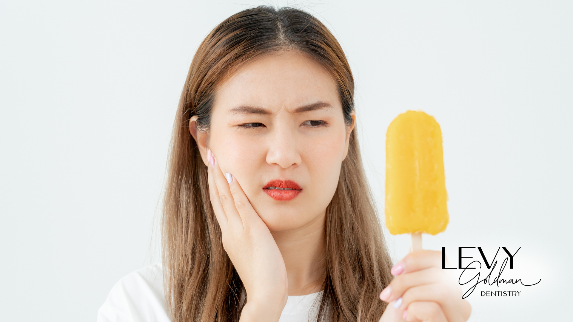 A woman is holding an ice cream bar and has a toothache.