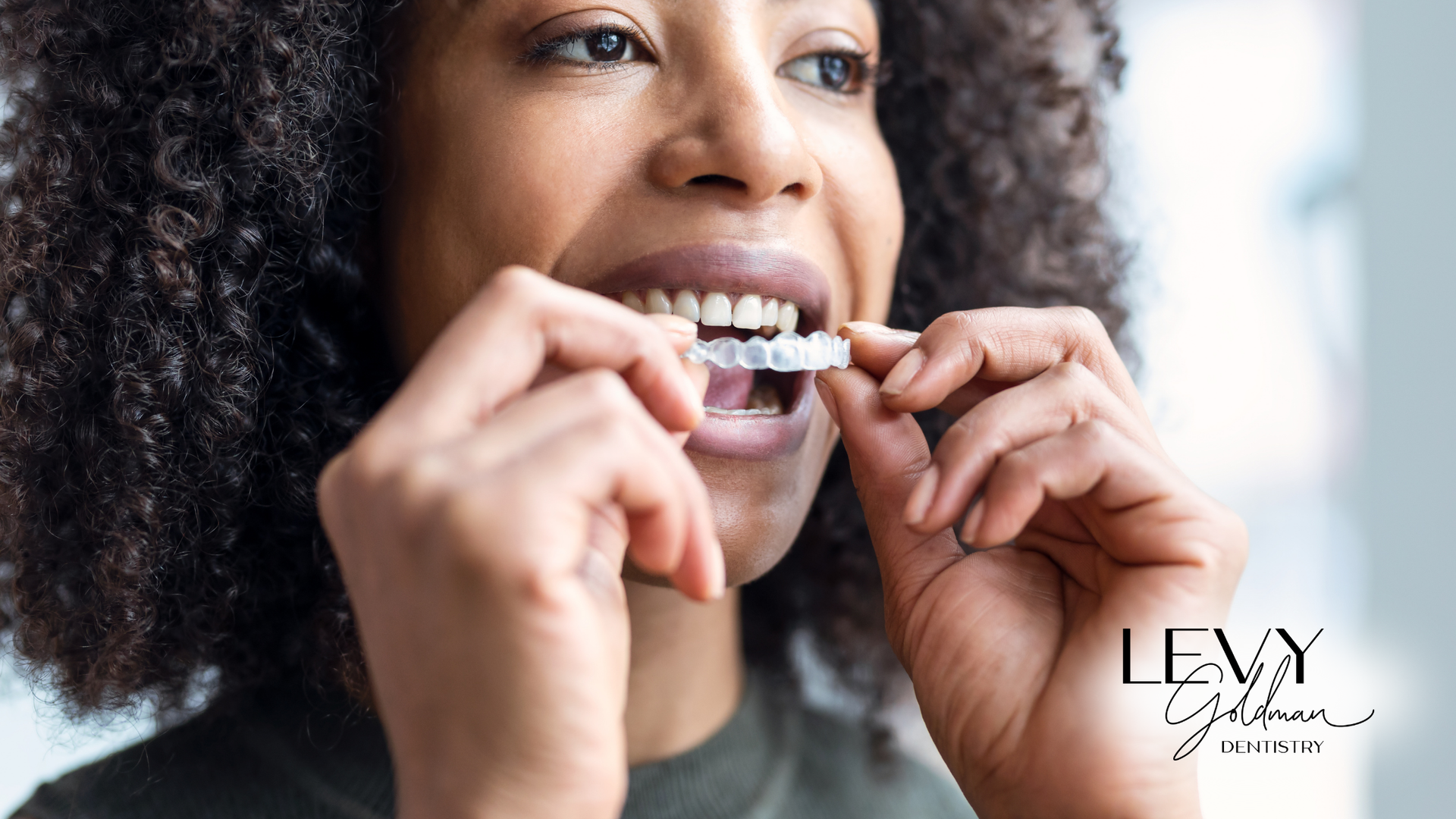 A woman is putting Invisalign in her mouth.