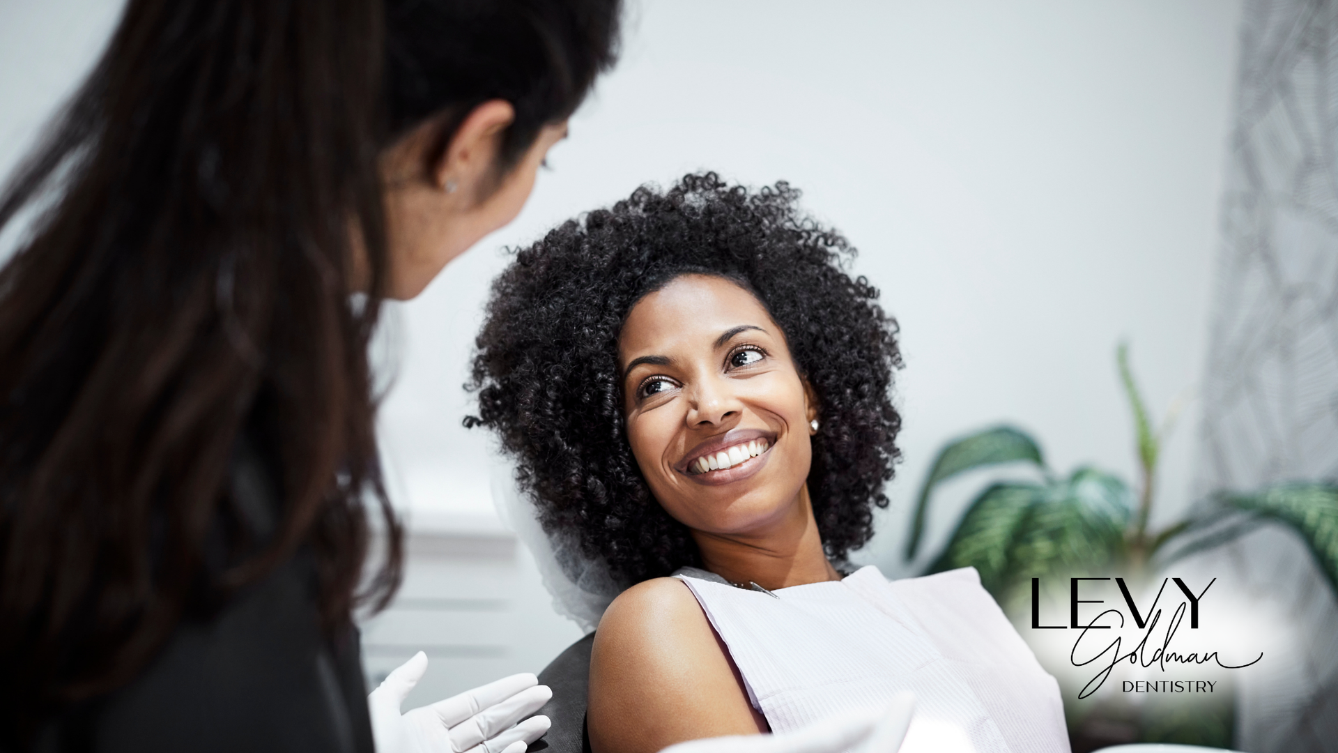 A woman is sitting in a dental chair talking to a dentist.