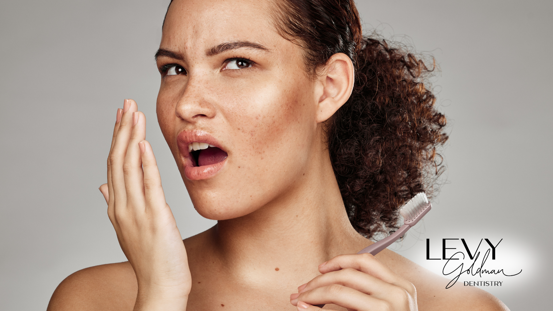 A woman is holding a toothbrush in her hand and covering her mouth.