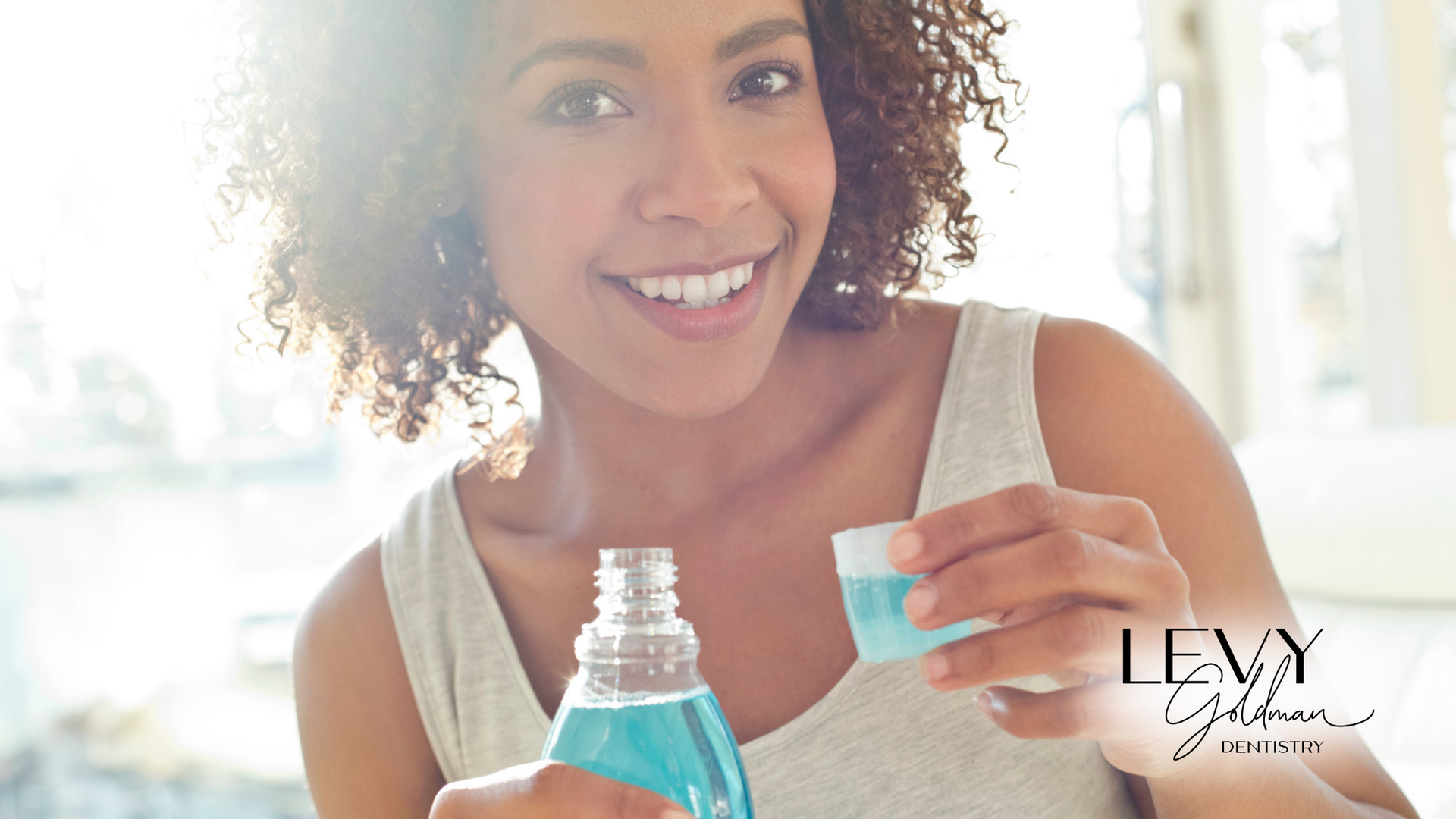 A woman is holding a bottle of mouthwash and smiling.