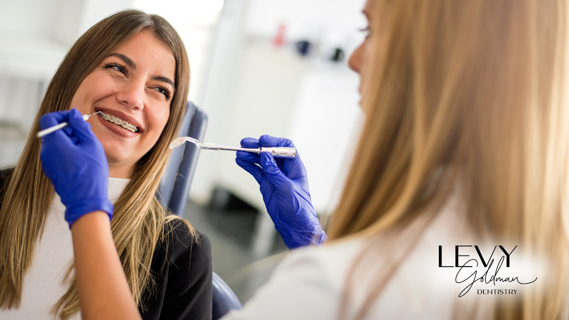 A woman with braces is getting her teeth examined by a dentist.