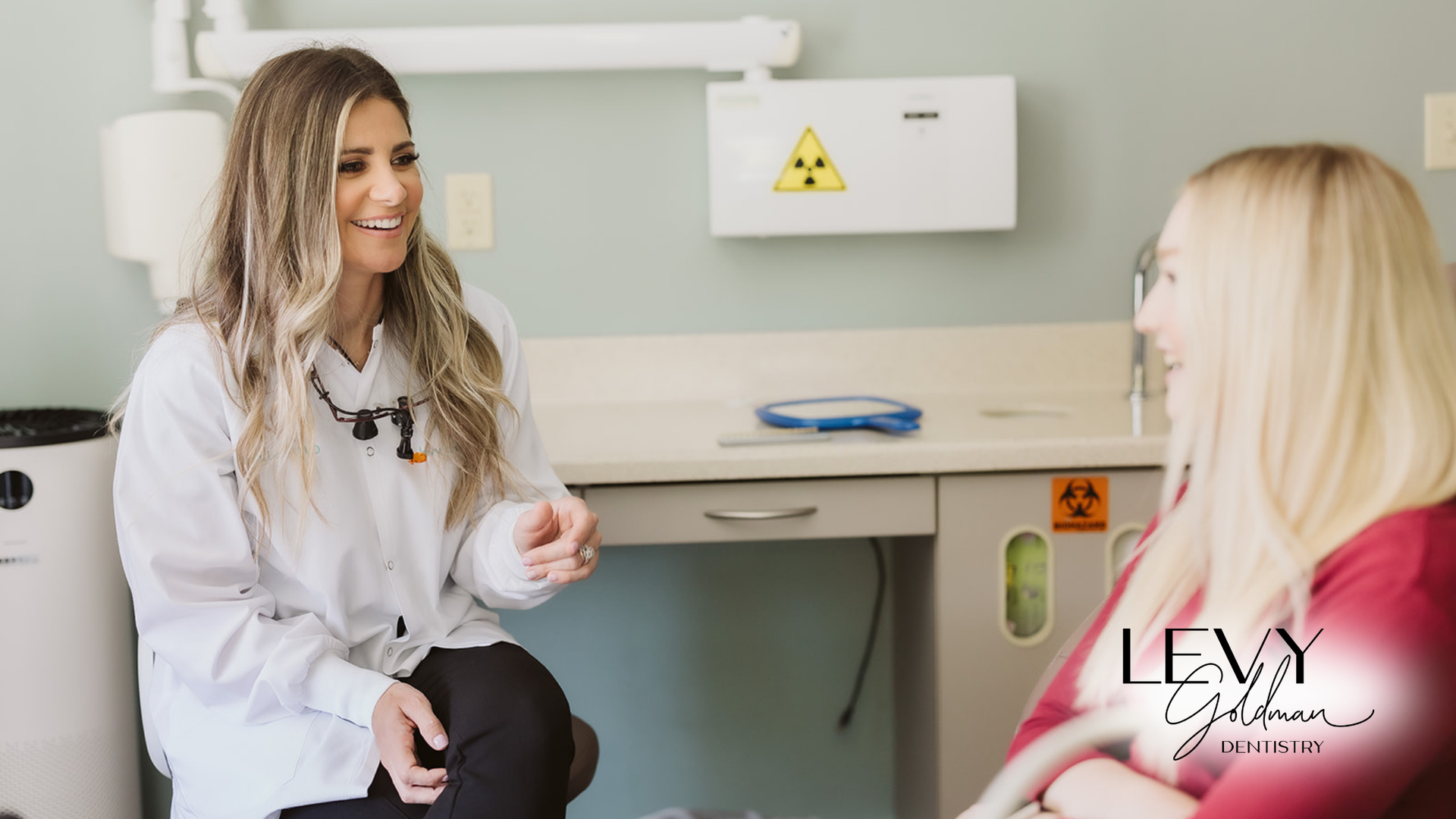 A dentist is talking to a patient in a dental chair.