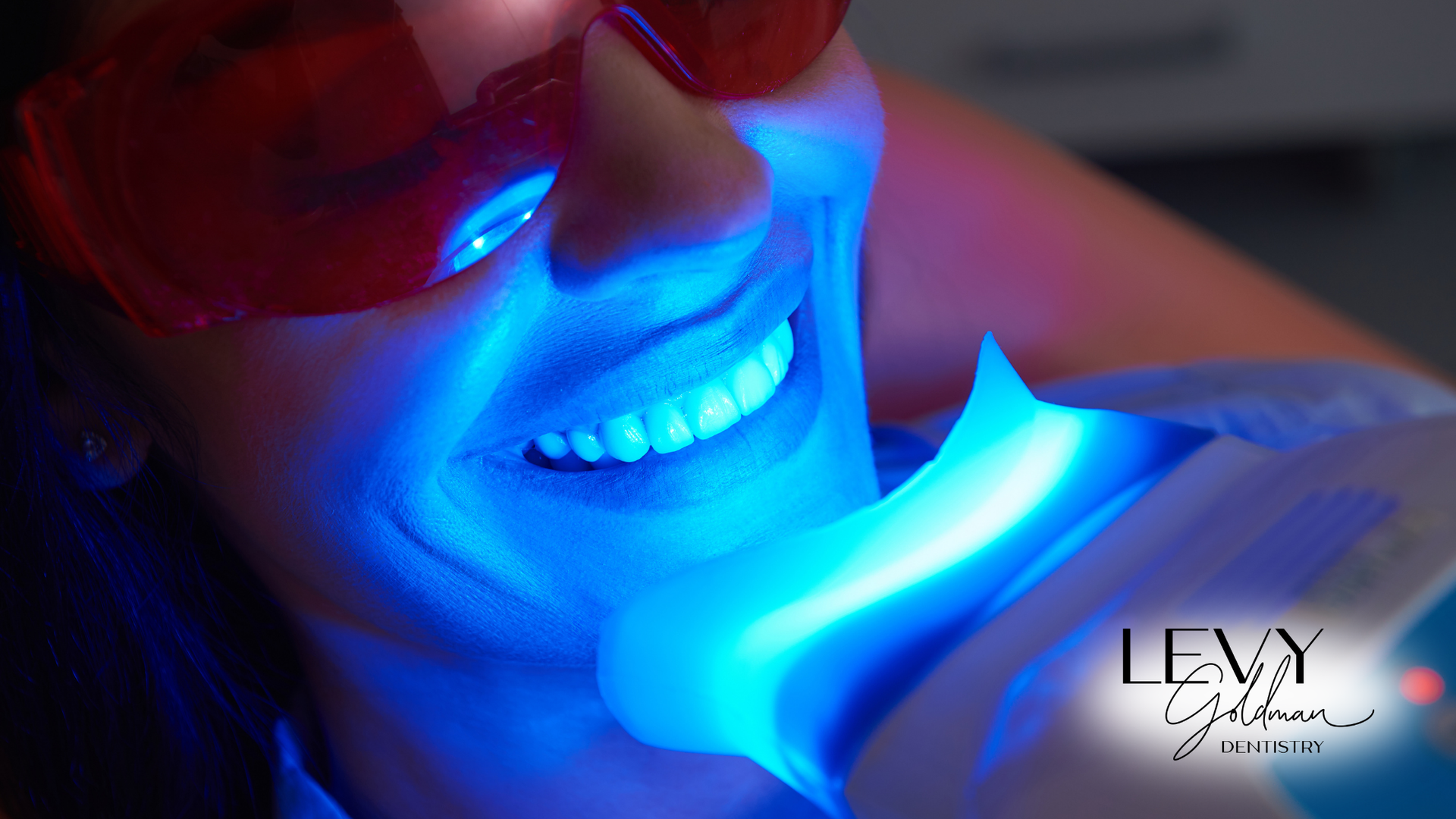 A woman is getting her teeth whitened with a blue light