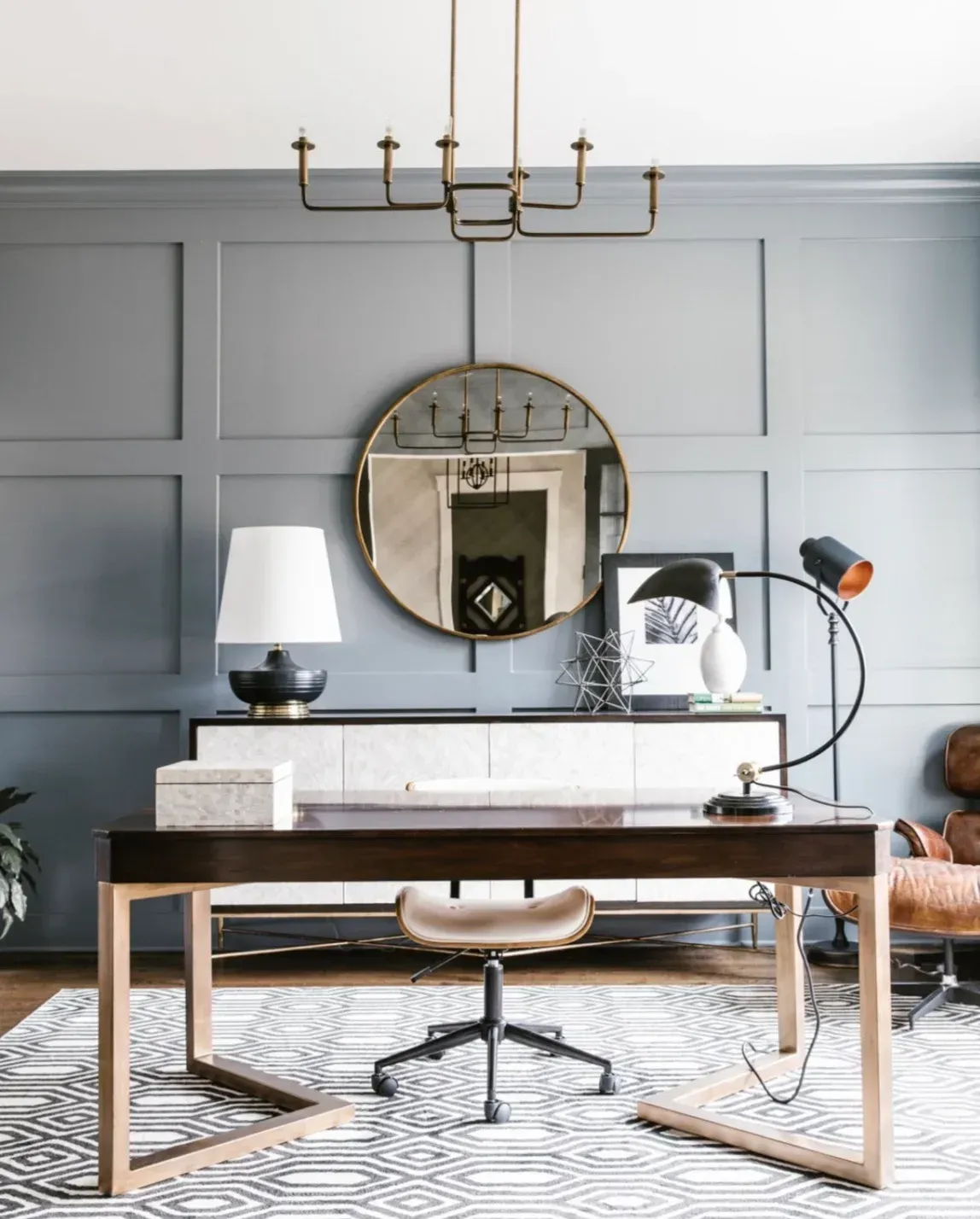 A home office with a desk , chair , lamp and mirror.