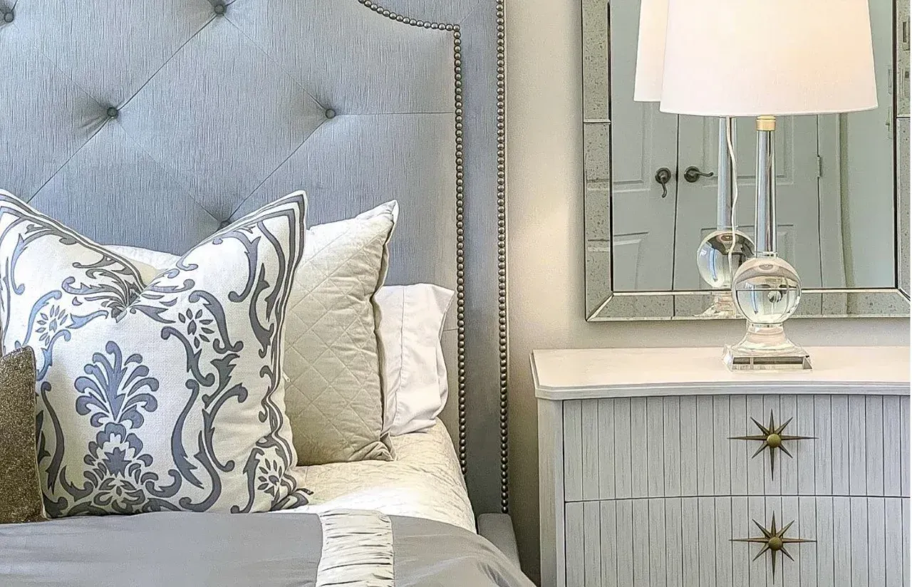 A bedroom with a bed , nightstand , mirror and lamp.