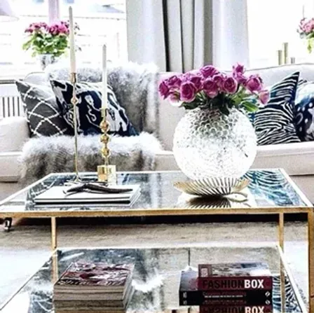 A living room with a glass coffee table and a vase of flowers on it.