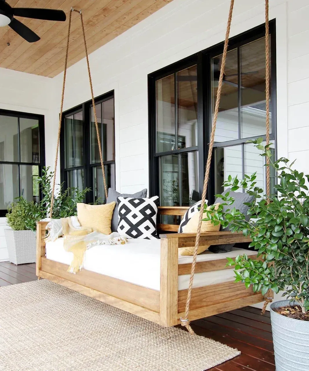A porch with a wooden swing and a ceiling fan.