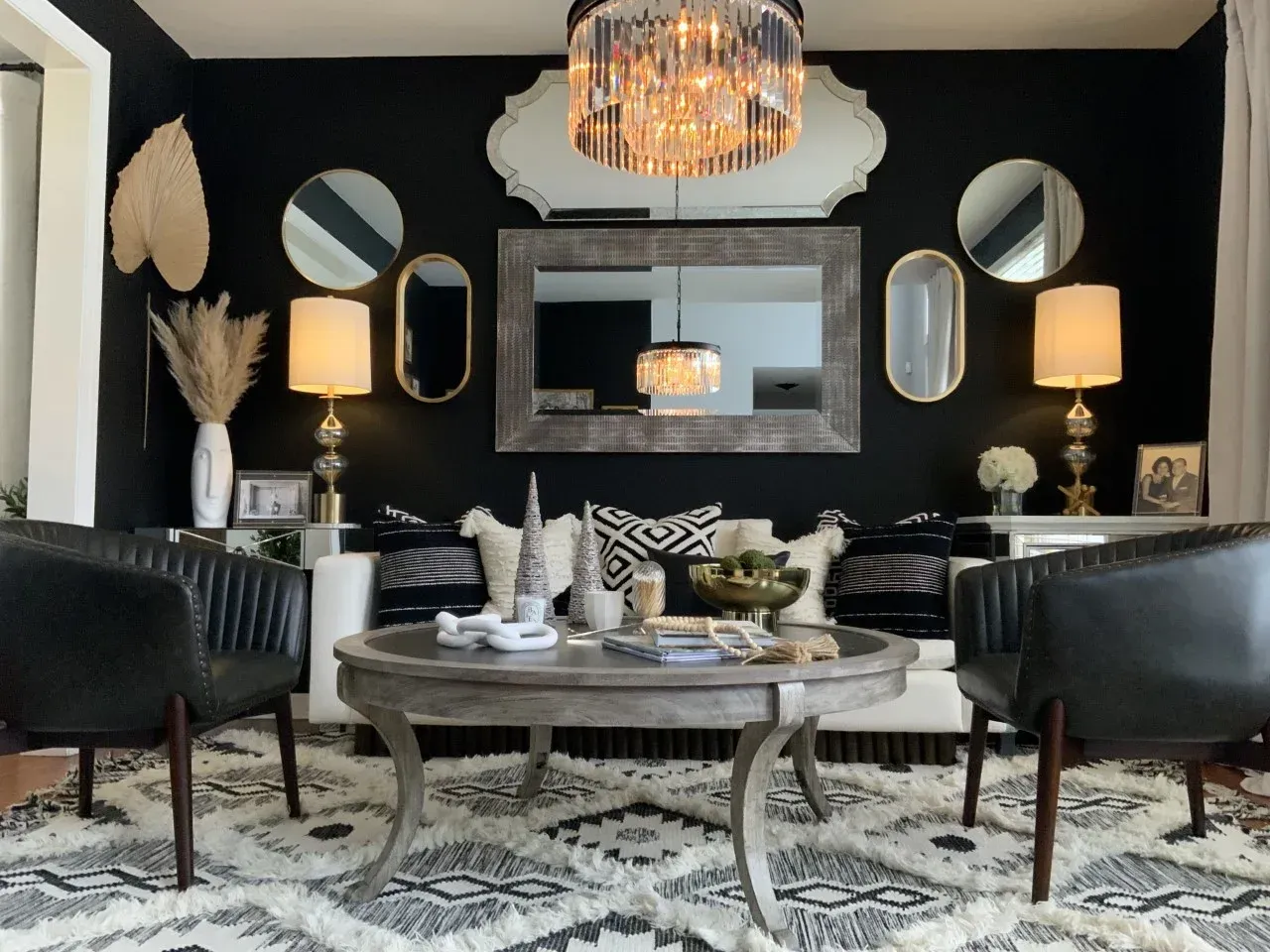 A living room with a couch , chairs , coffee table and mirrors.
