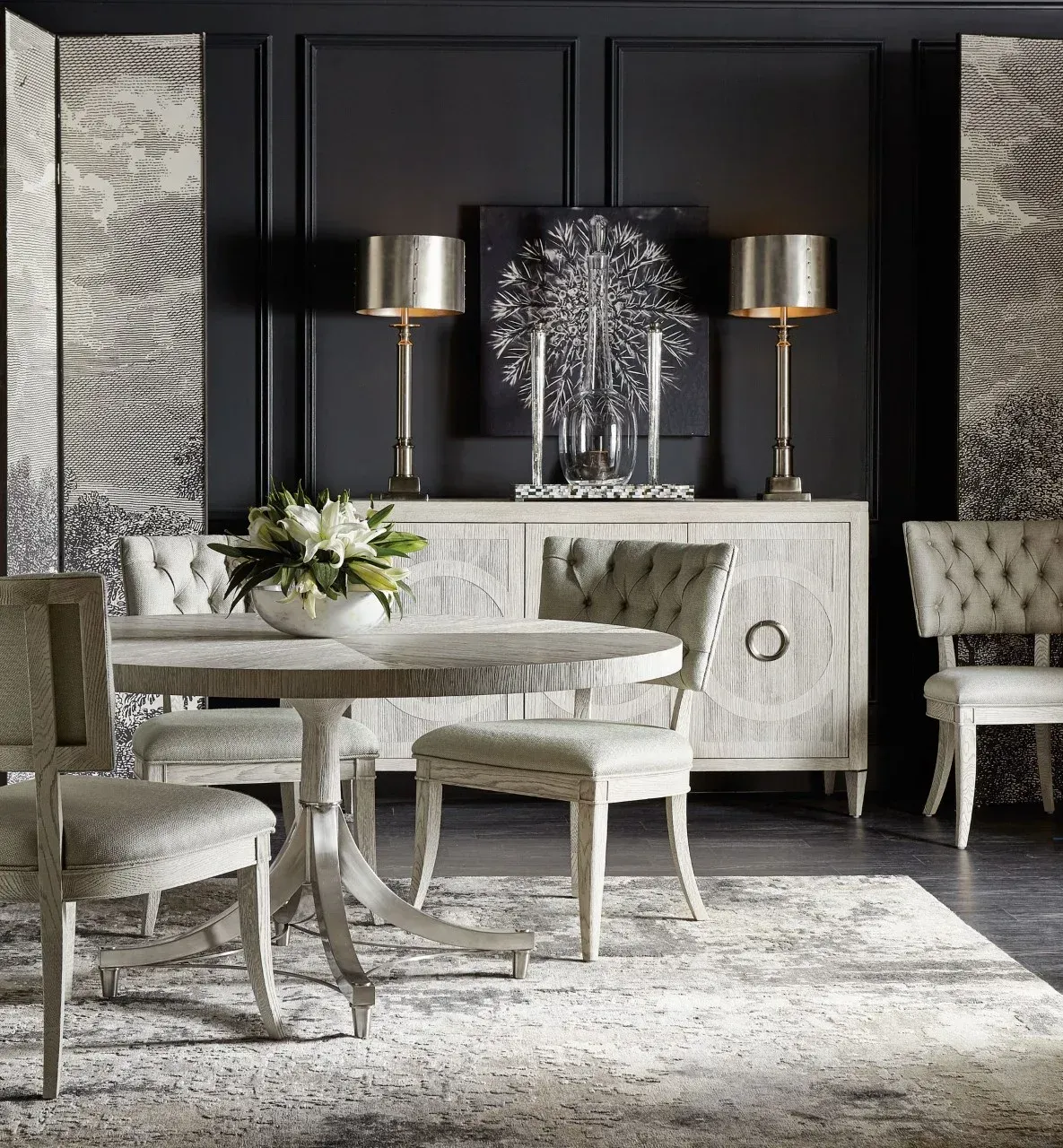 A dining room with a table , chairs , lamps and a vase of flowers.