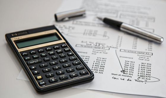 Calculator, pen, and financial papers on a white surface, suggesting accounting or financial analysis.