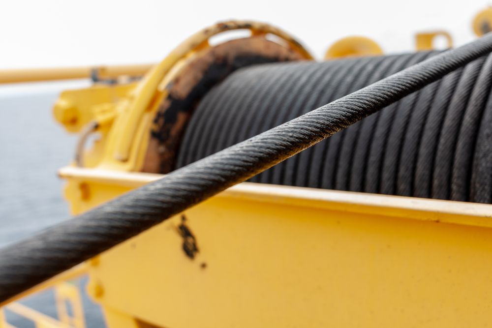 Close-up of a thick, black steel cable extending from a yellow winch. The cable has a ridged texture.